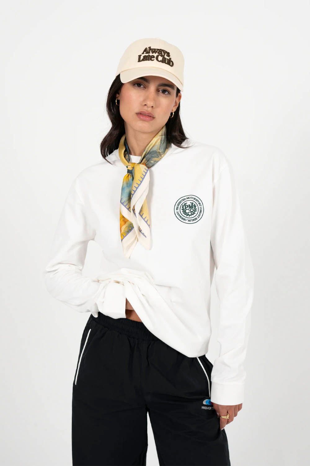 Person wearing a white jacket with a logo, black pants, and a beige cap on a white background