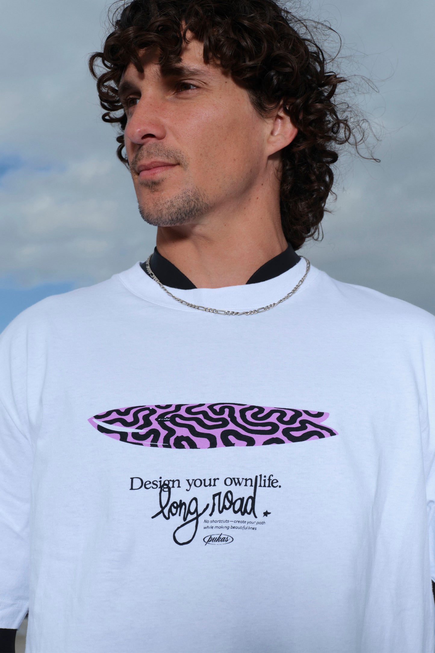 Person wearing a white t-shirt with a purple graphic and text against a cloudy sky.