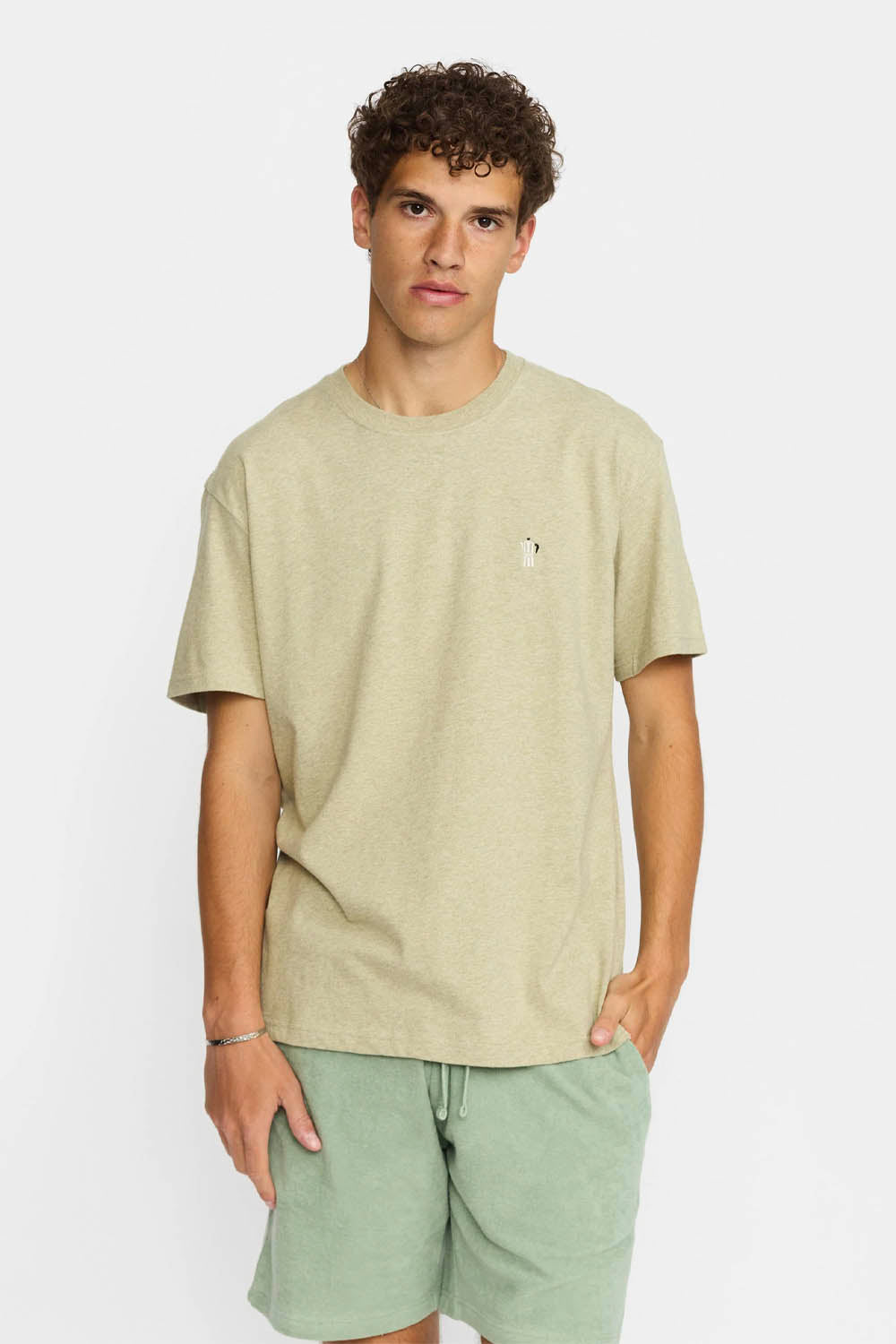Man wearing a beige t-shirt and light green shorts on a white background