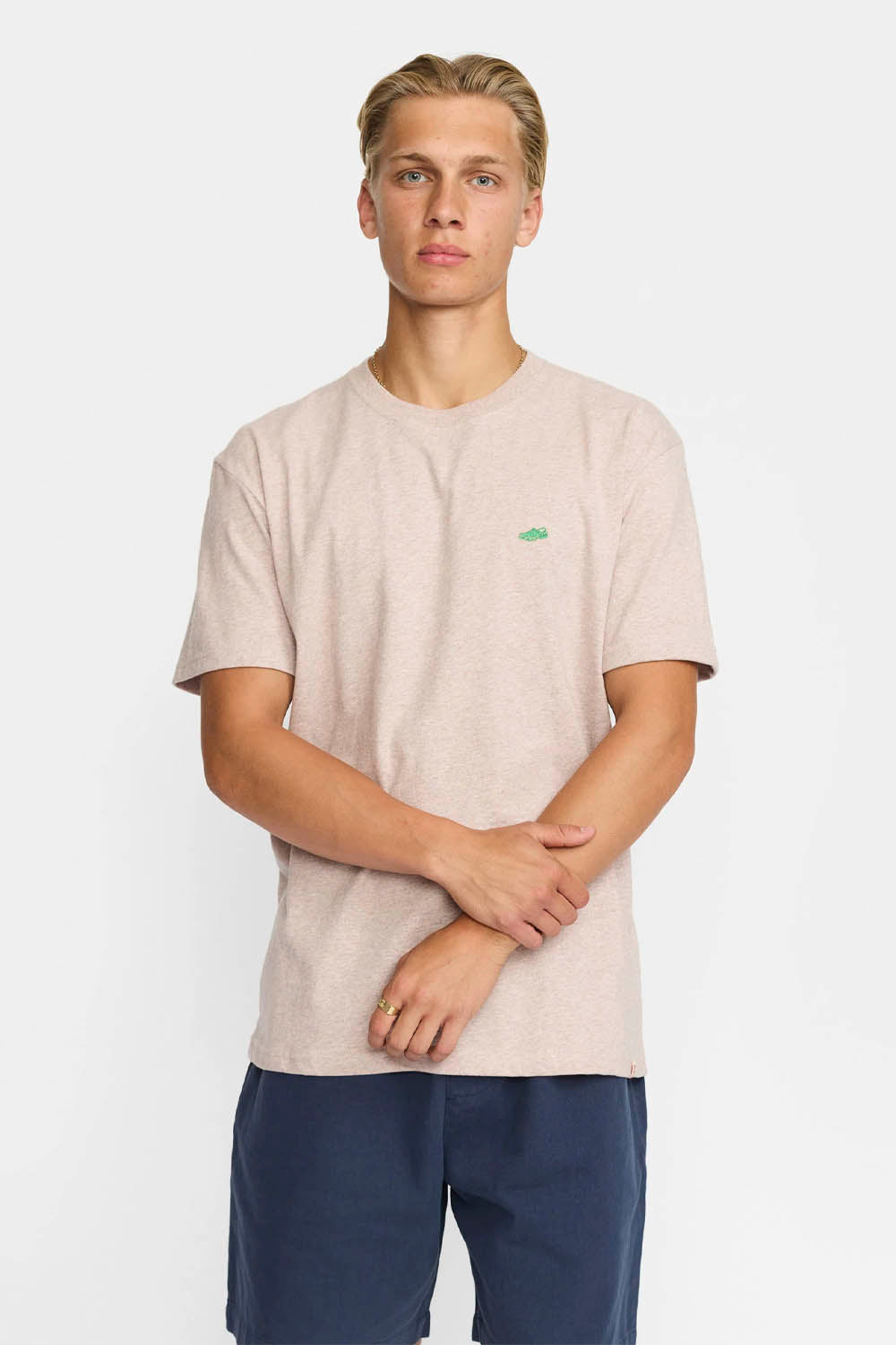 Man wearing a beige t-shirt with a small green graphic on a white background
