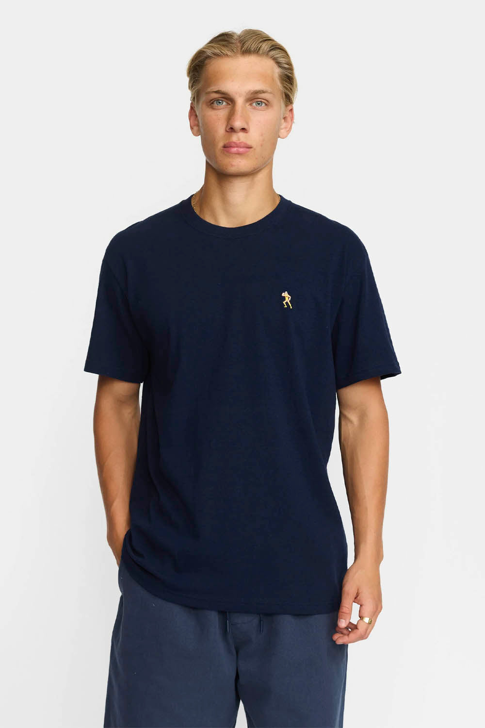 Man wearing a navy blue t-shirt with a small logo on a white background