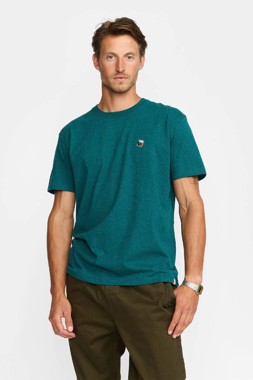 Man wearing a teal t-shirt with a small logo on a white background