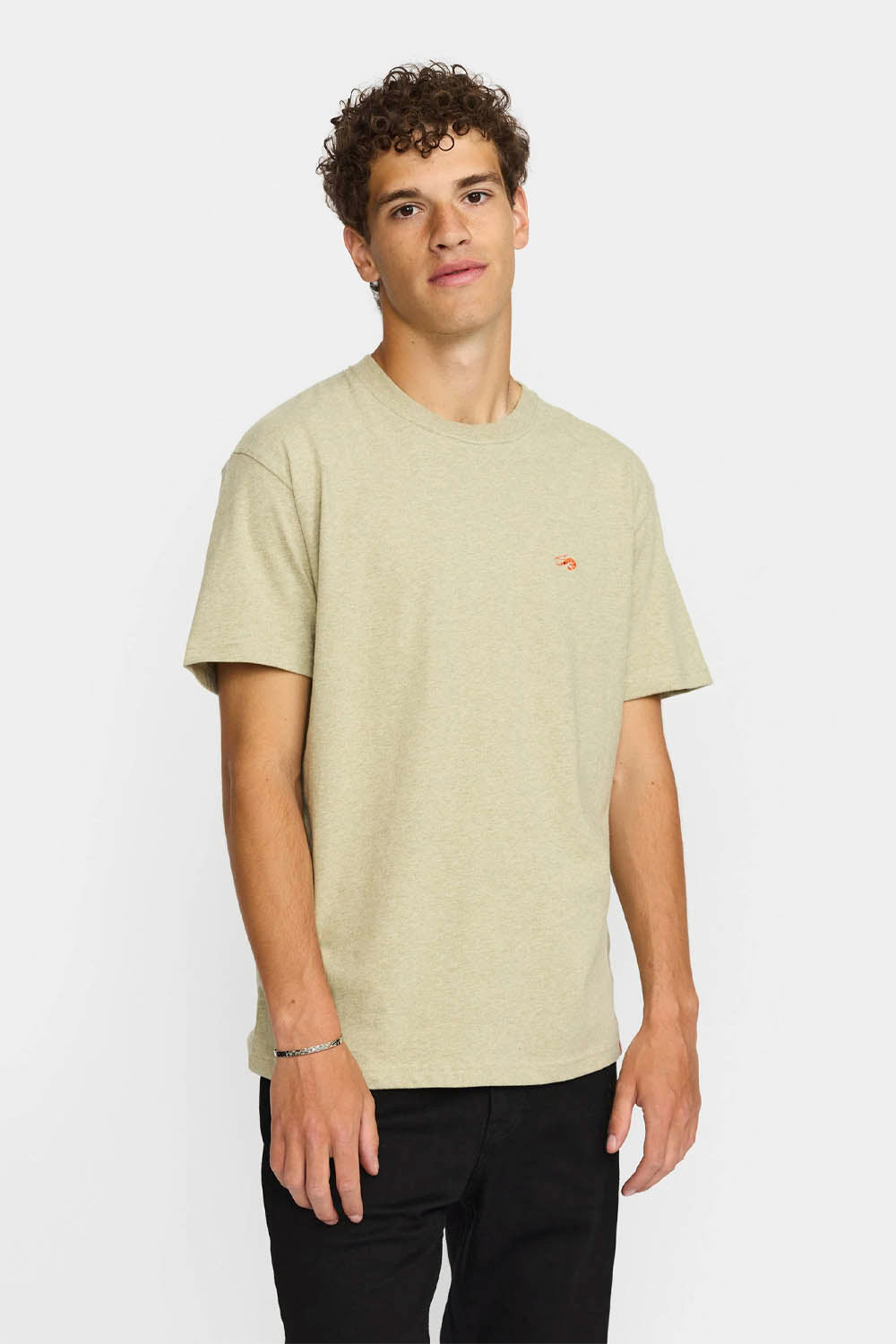Man wearing a beige t-shirt with a small logo on a white background