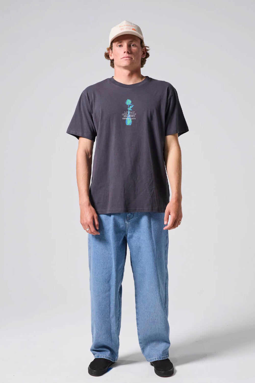 Person wearing a dark t-shirt with a graphic design and light blue jeans on a white background