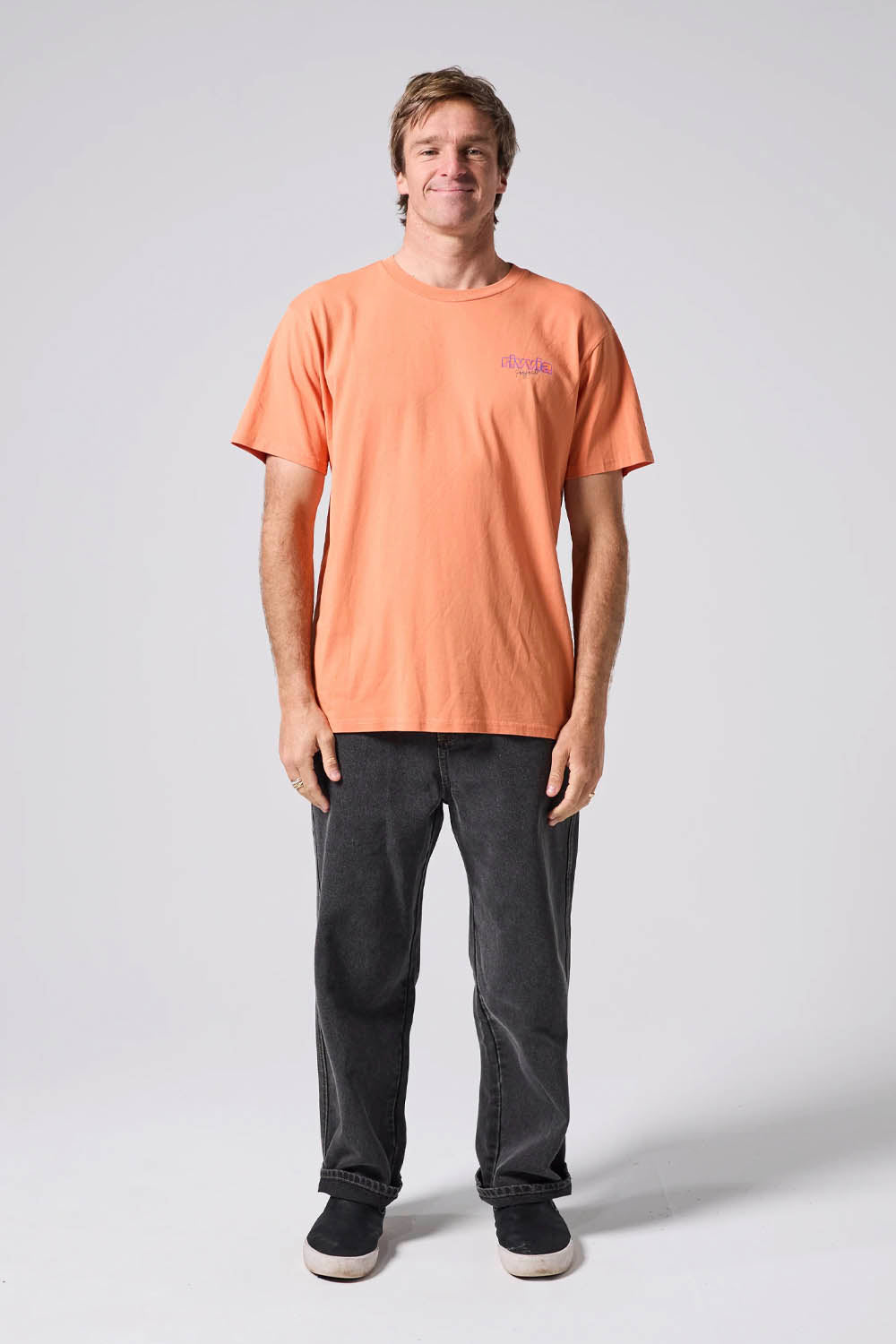 Person wearing an orange t-shirt and dark jeans on a white background