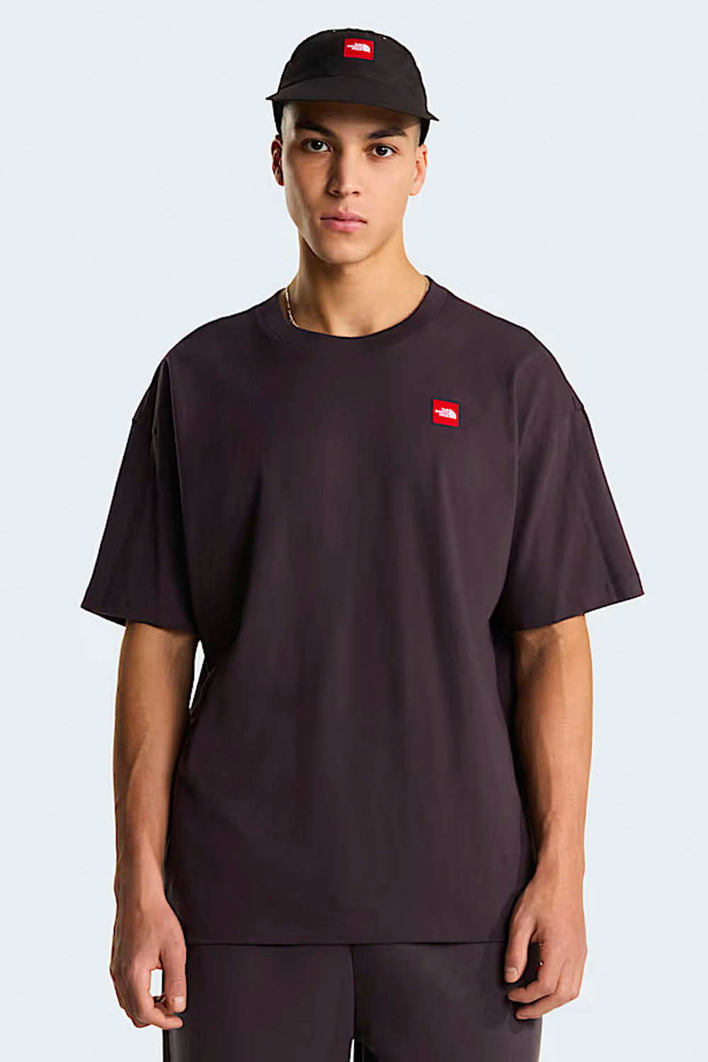Person wearing a black t-shirt with a red logo and a black cap on a white background