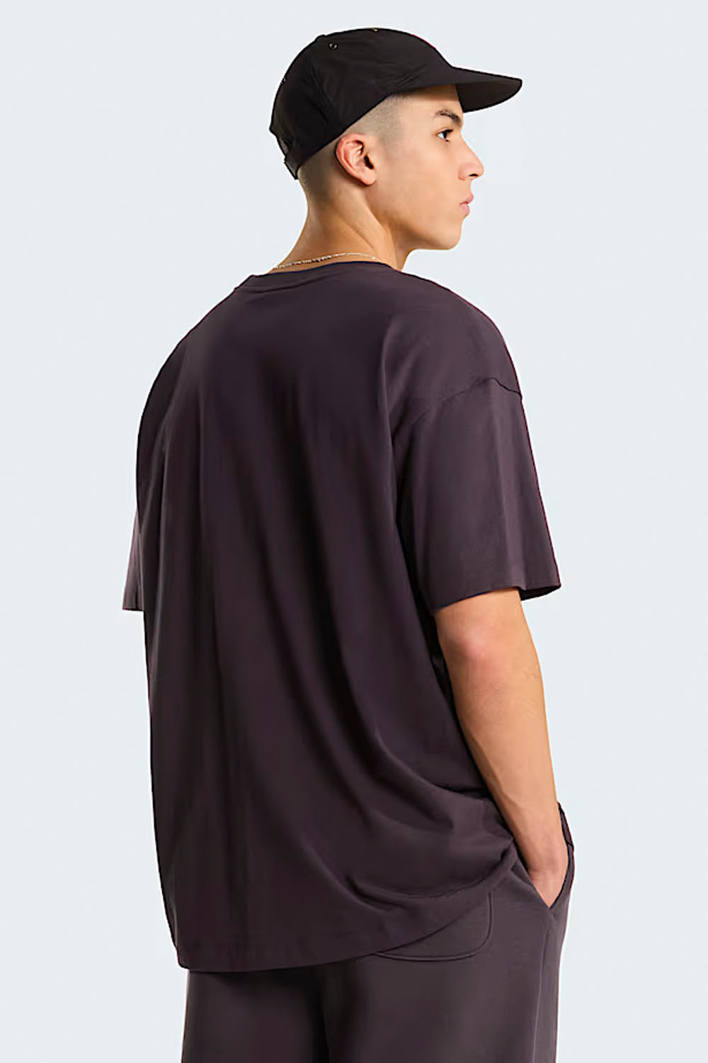 Person wearing a dark brown t-shirt and cap on a light gray background