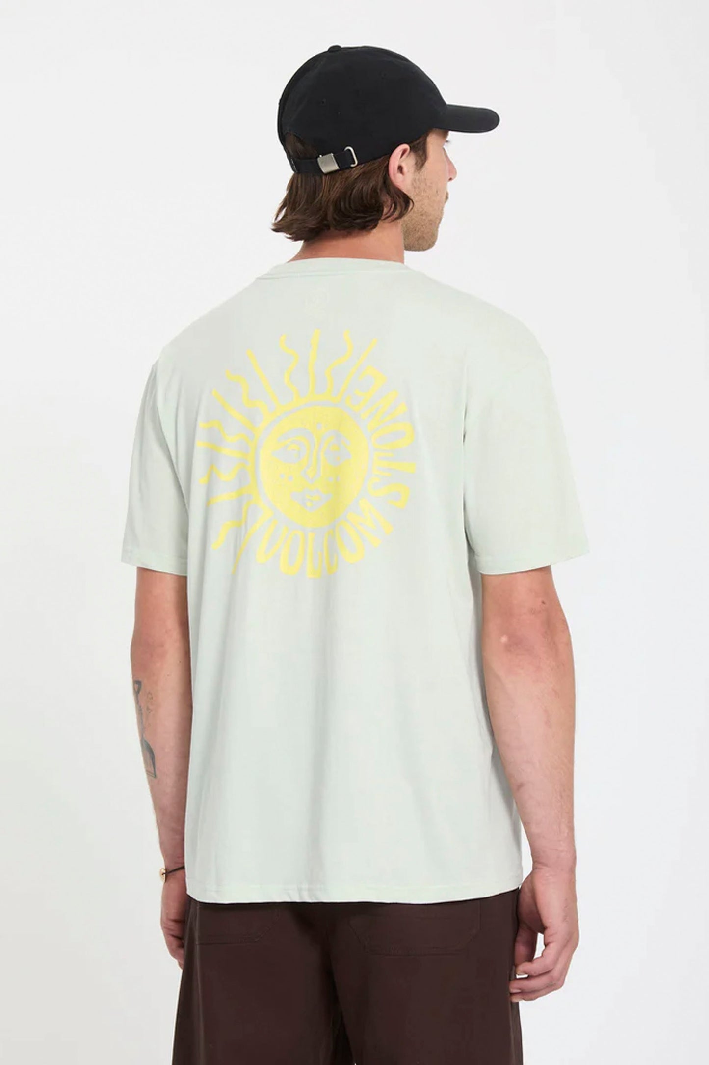 Person wearing a light green Volcom Mazatlan t-shirt with a yellow sun design on the back, standing against a white background.