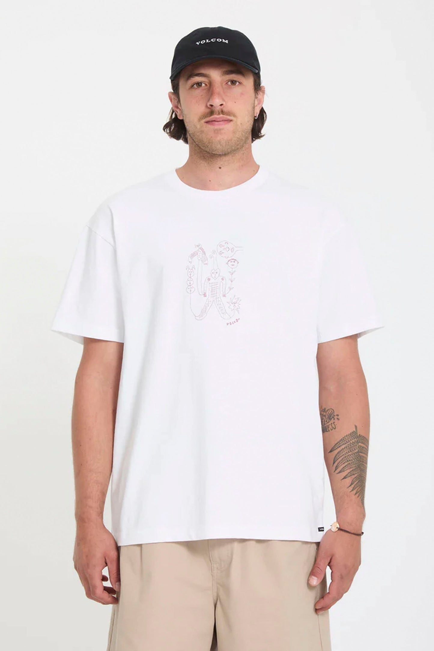 Man wearing a white Volcom Nowhere t-shirt with a graphic design and a black cap on a plain background