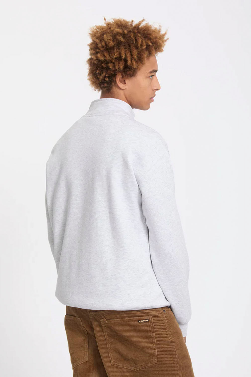 A man with curly light brown hair, seen from the back, wearing a light gray heathered quarter-zip sweatshirt and brown corduroy pants against a plain white background.
