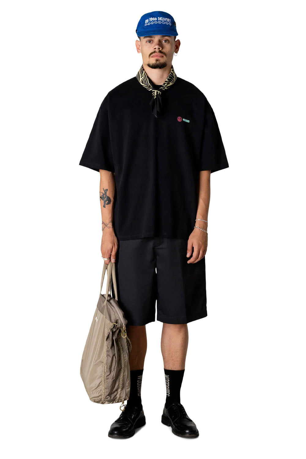 Person wearing a black outfit with a blue cap and carrying a beige bag on a white background