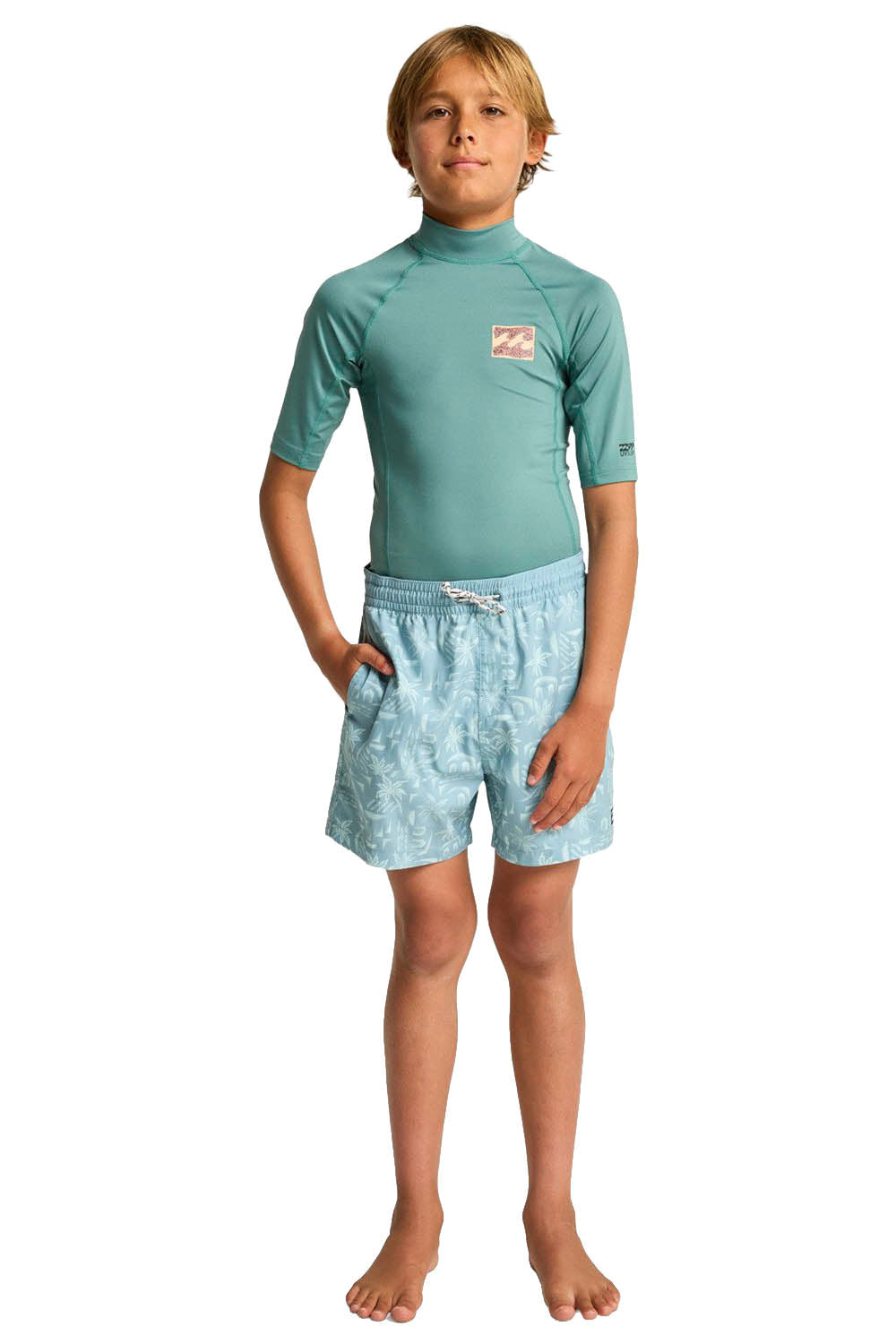 Child wearing a green rash guard and light blue swim shorts on a white background
