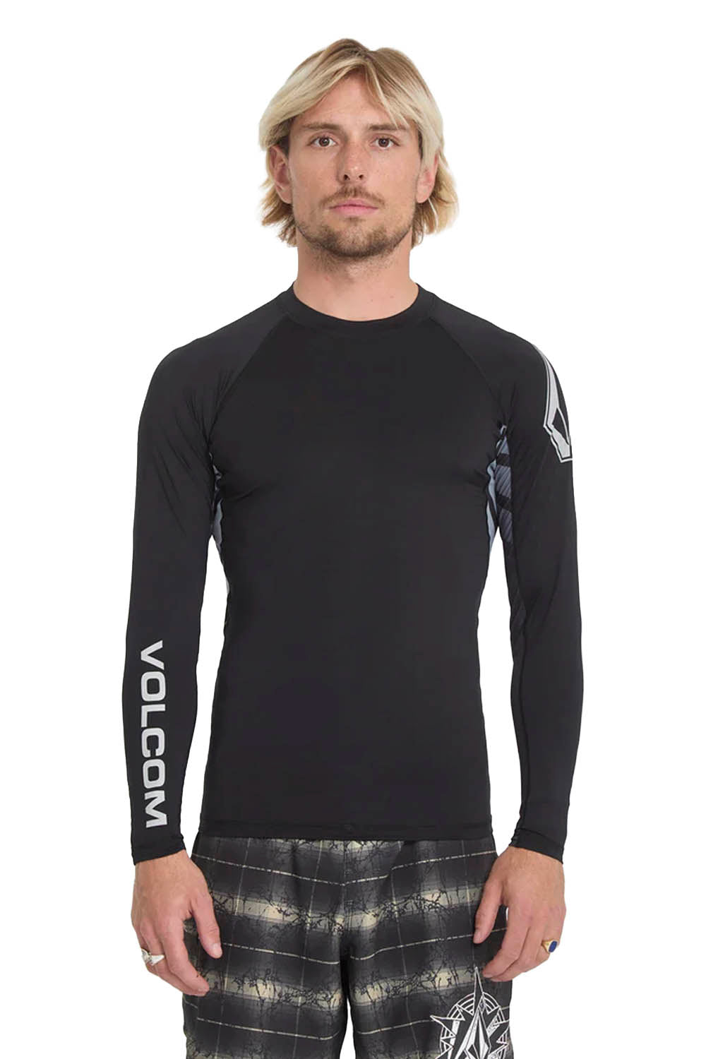 Man wearing a black Volcom long-sleeve rashguard and patterned shorts on a white background