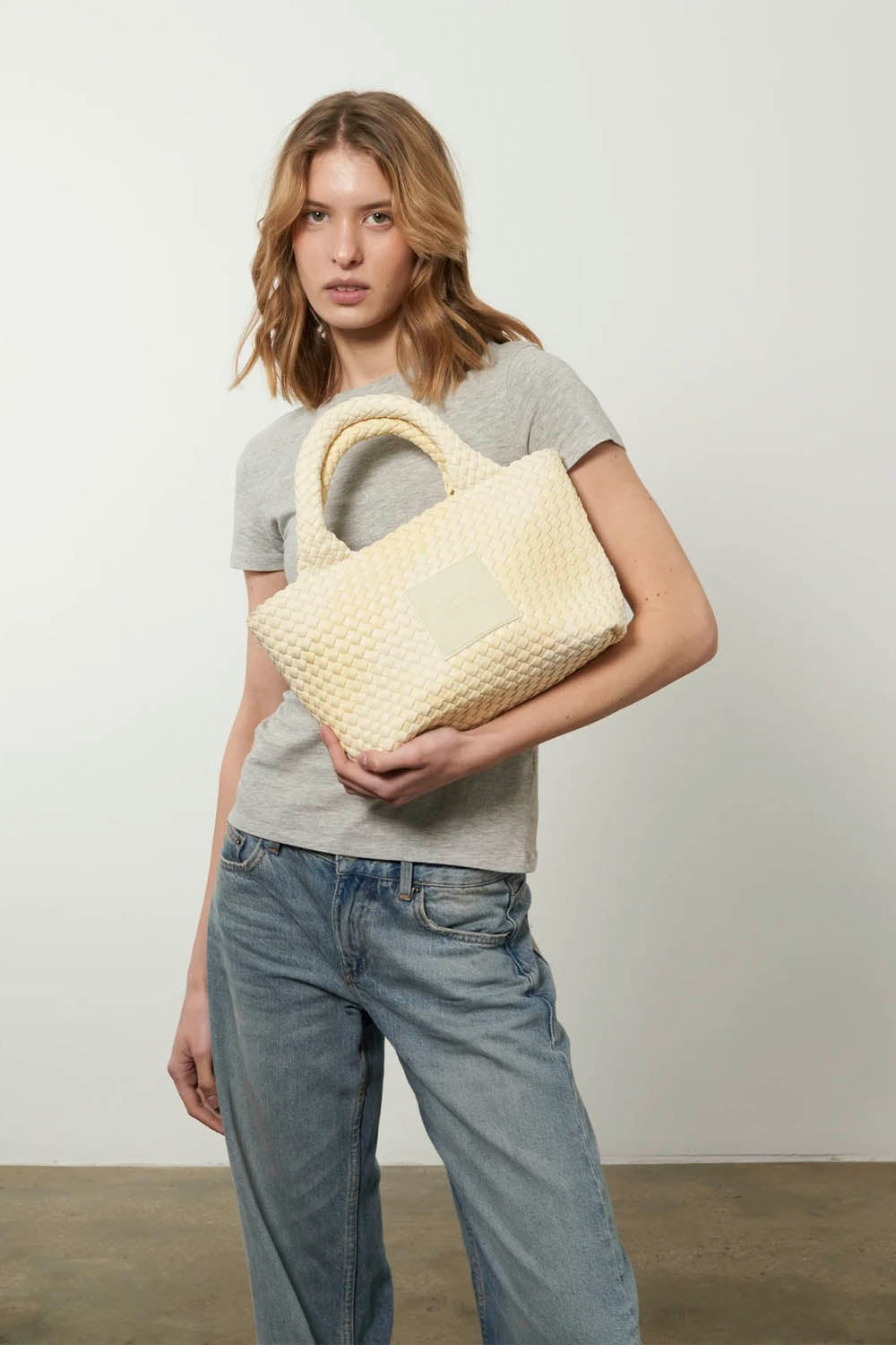 Woman holding a woven beige bag against a plain background