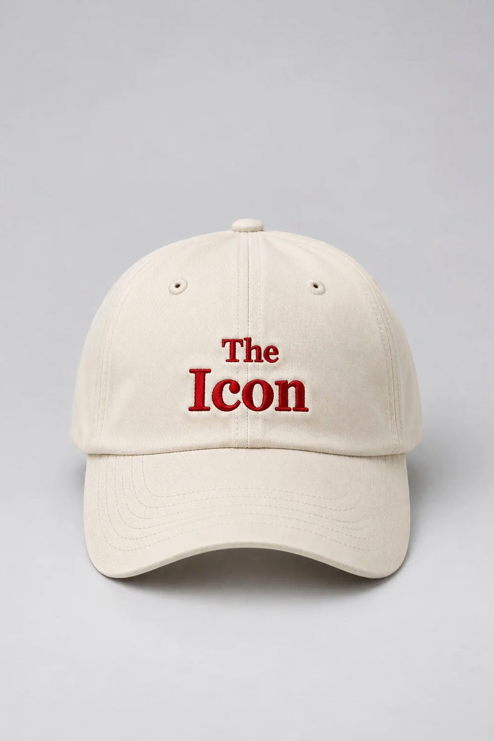 An off-white baseball cap with 'The Icon' embroidered in red on the front, set against a neutral gray background.
