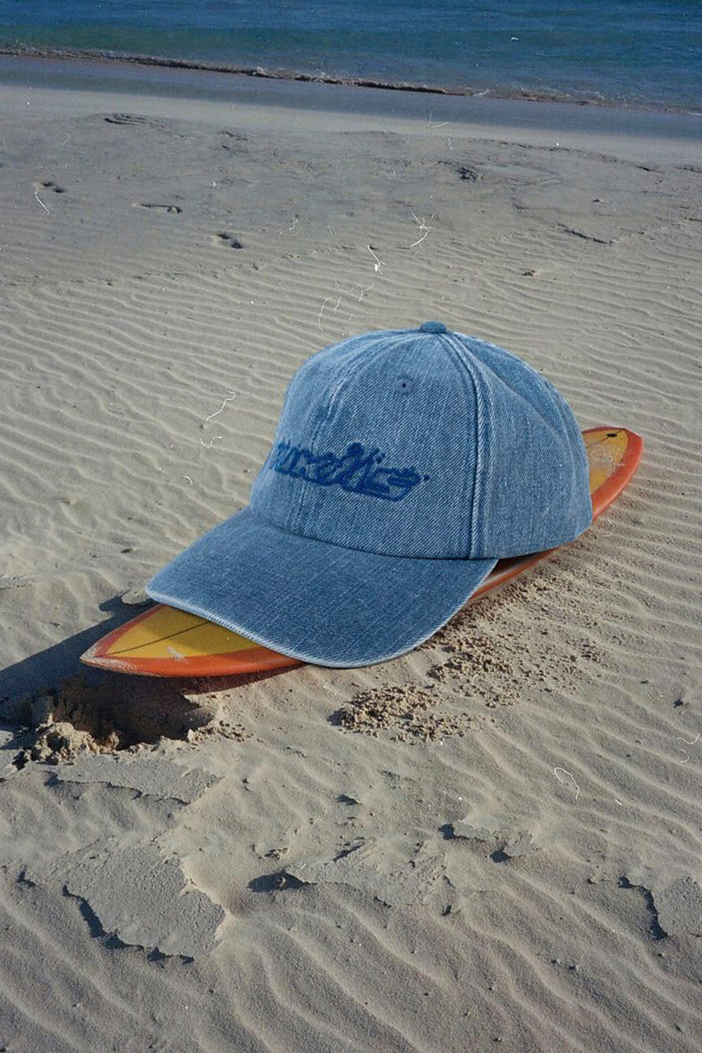 Blue cap with 'Barnett' logo on a surfboard in the sand
