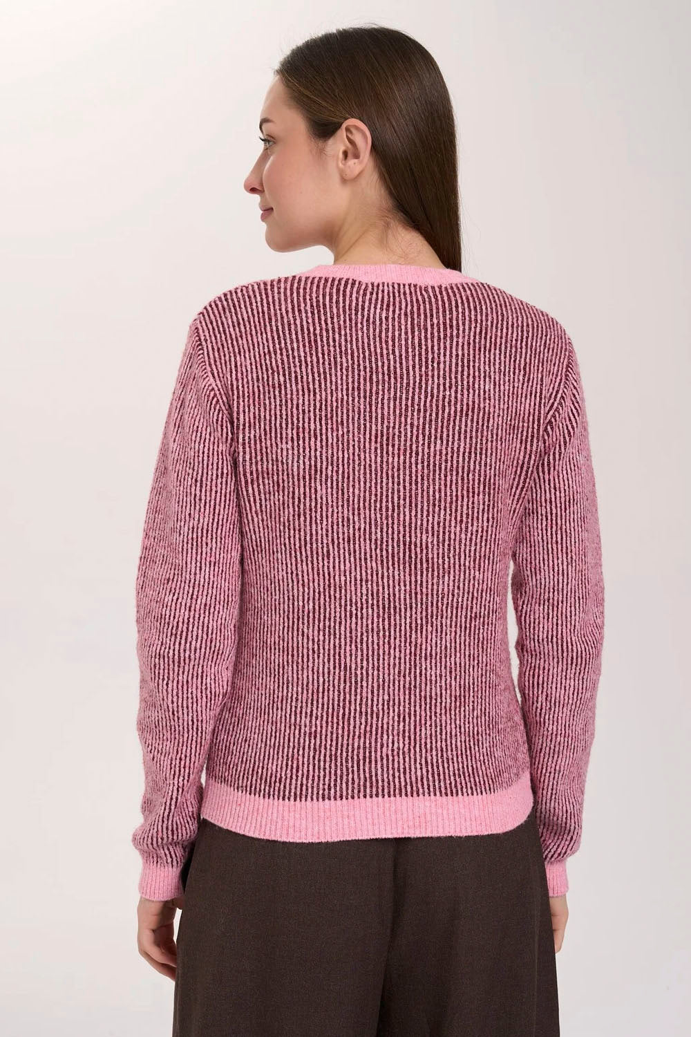 A woman shown from the back wearing a pink and mauve marled ribbed knit sweater with light pink trim, paired with dark brown pants, against a plain light background.