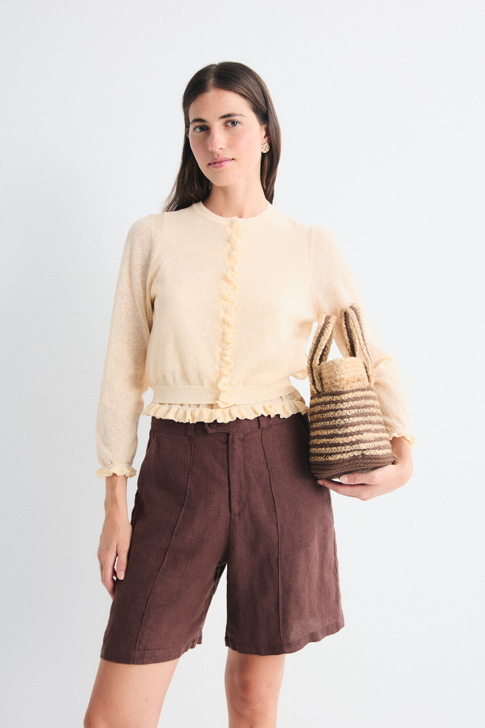 Woman wearing a yellow cardigan and brown pants on a plain background.