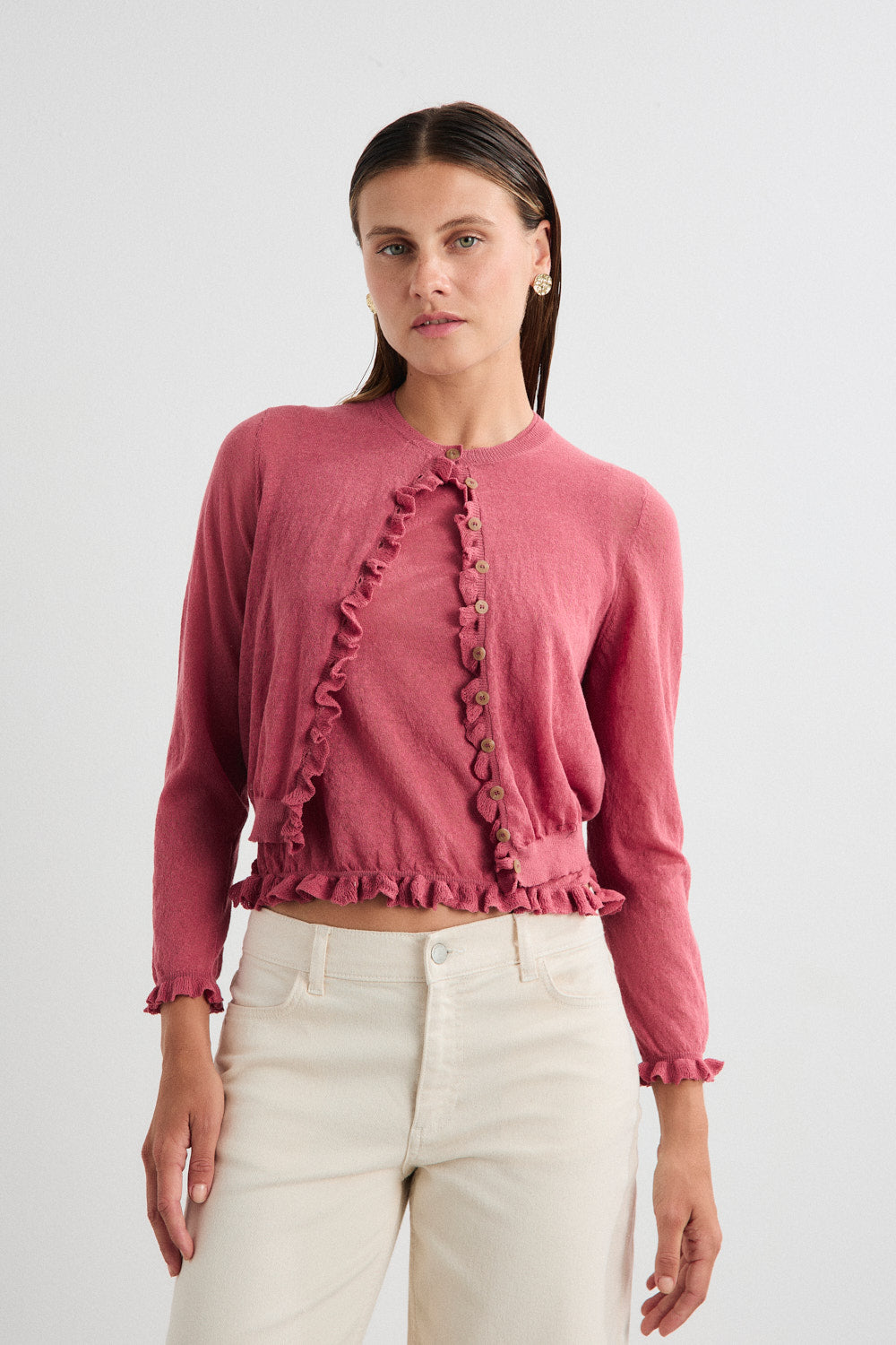 Woman wearing a pink cardigan with ruffled details on a white background