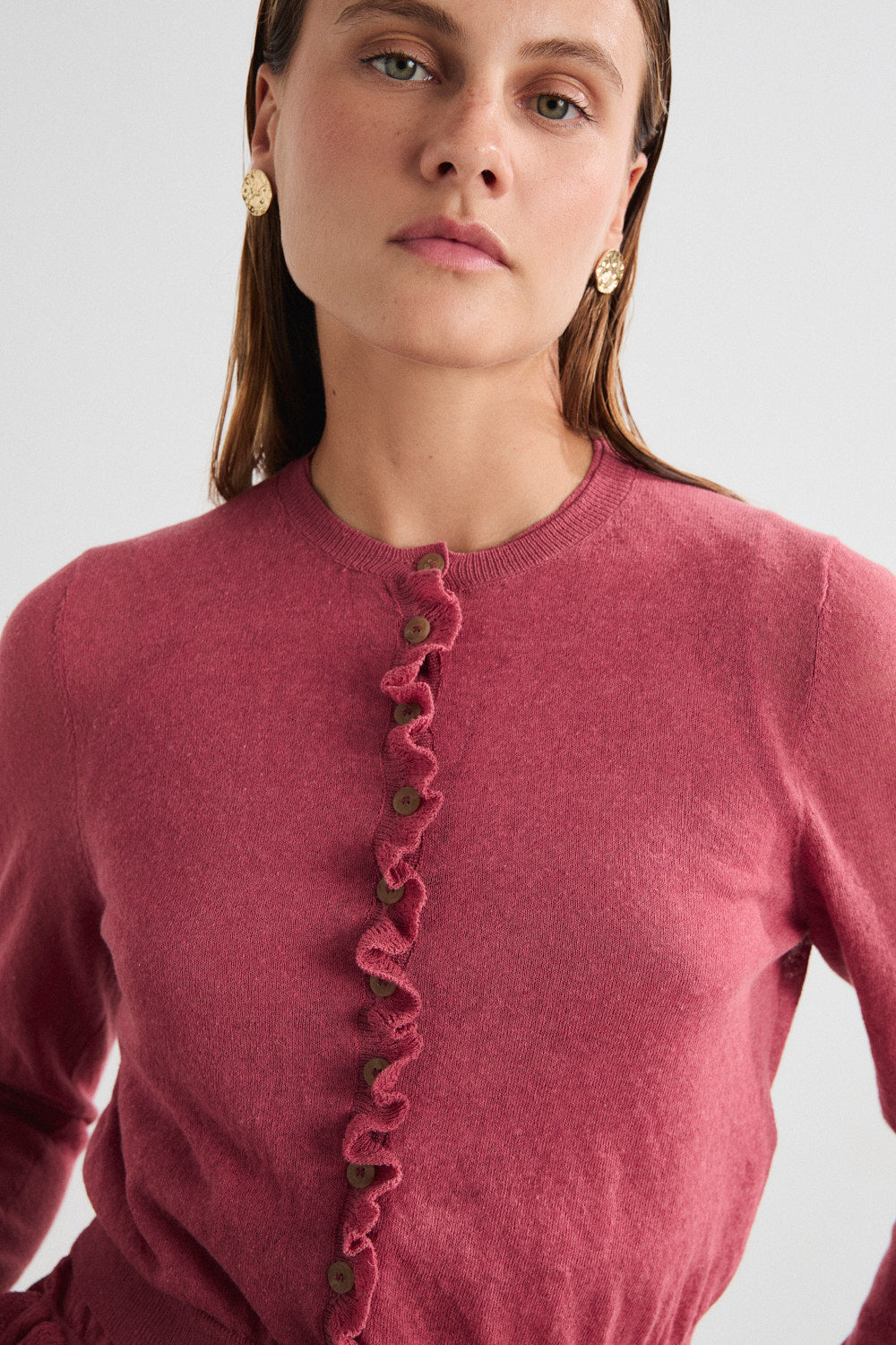 Woman wearing a pink cardigan with ruffled details on a white background