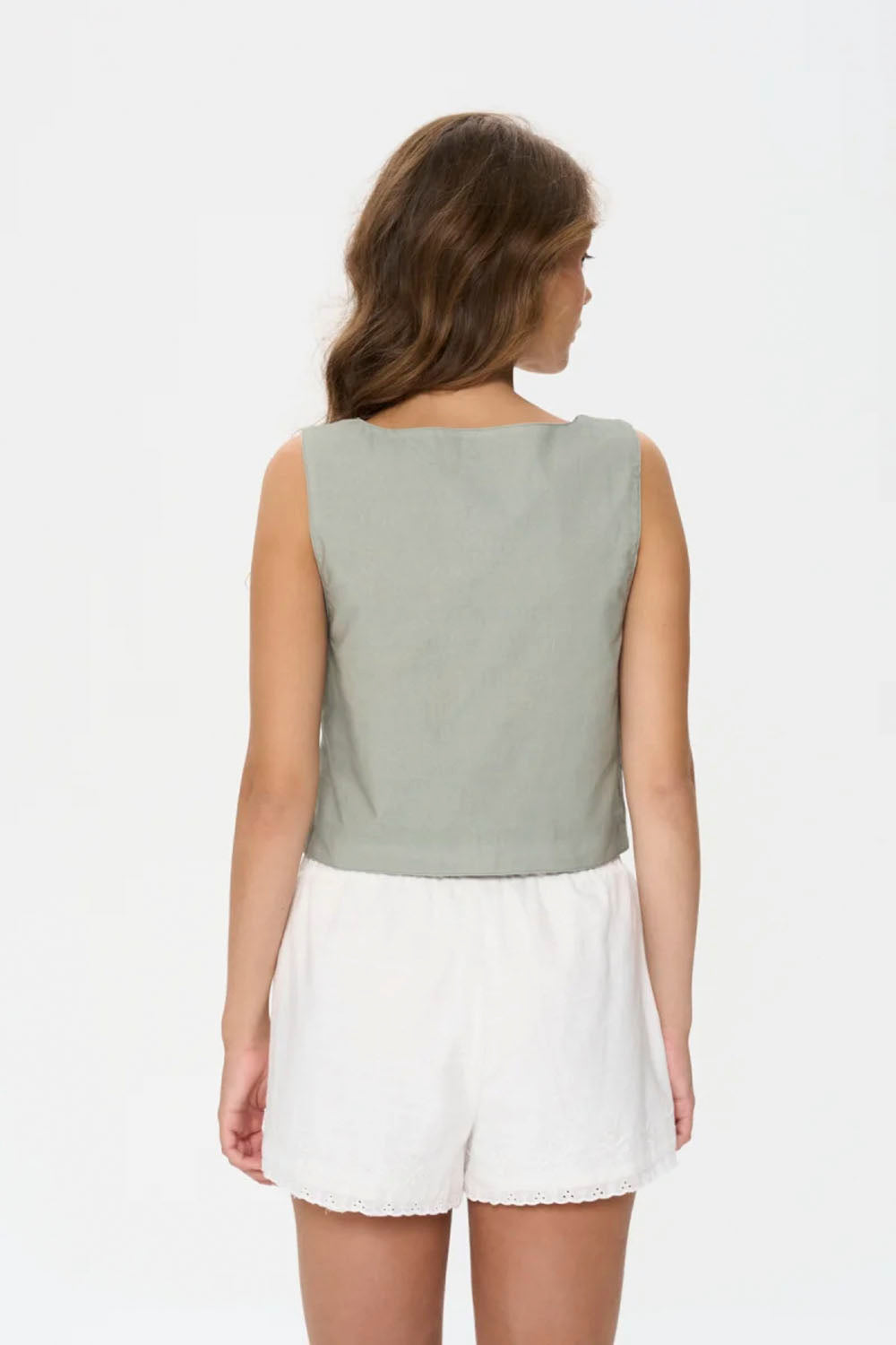 Woman wearing a light green sleeveless top and white shorts on a white background