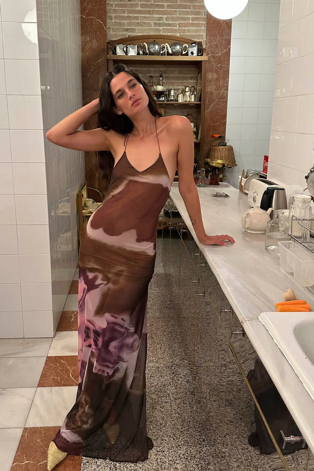 Woman in a long, patterned dress standing in a kitchen.