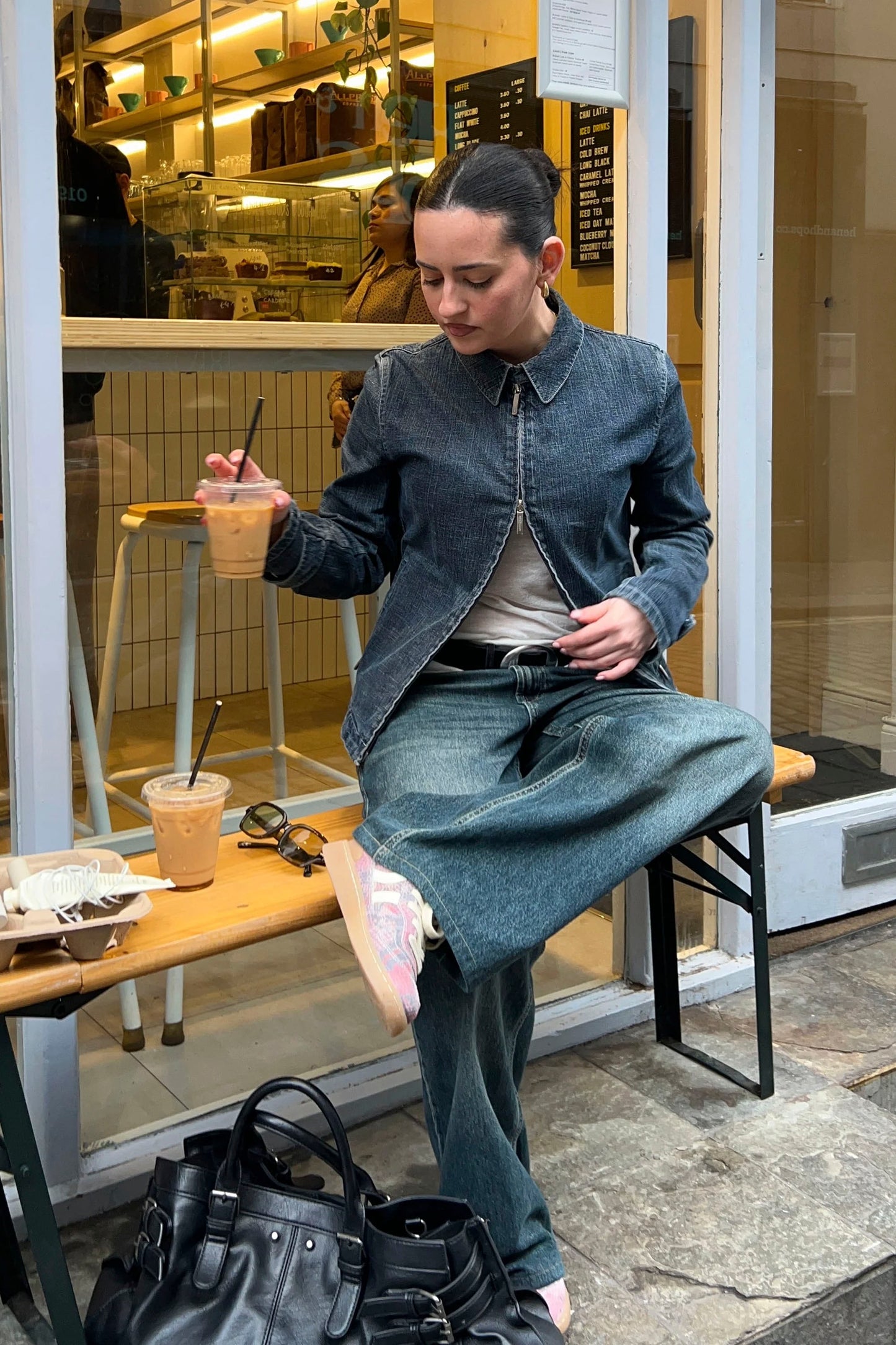 Person sitting on a stool in front of a store window, holding a drink amnd wearing Coolway Goal Pink Mamba sneaker.