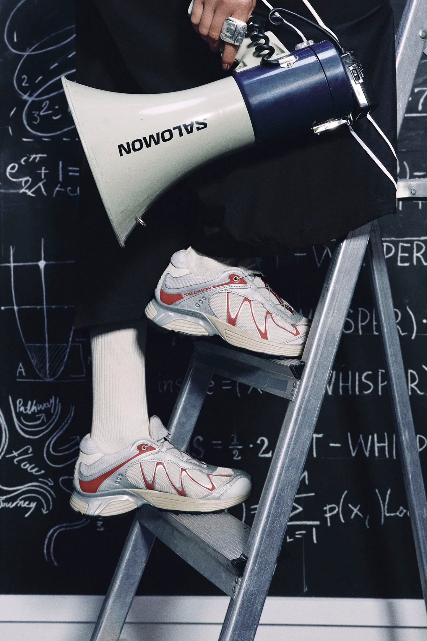 Person wearing Salomon XT-Whisper Silver Almond Milk women's sneaker on a step stool in front of a blackboard with mathematical equations.