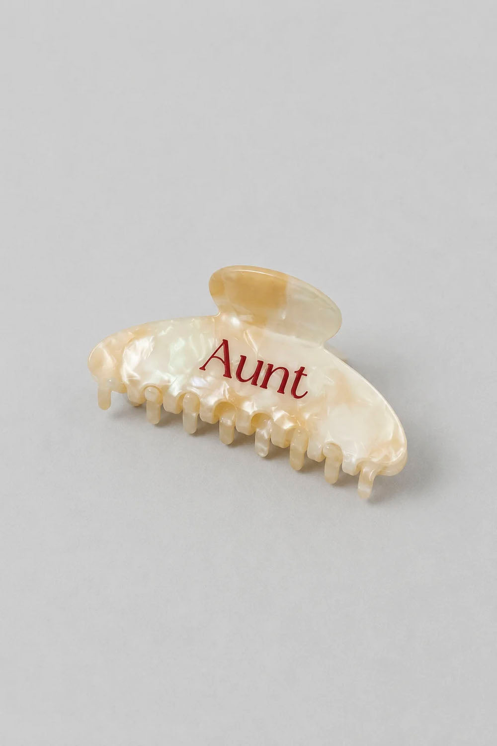A single hair claw clip in a pearlescent cream shell-like finish with the word 'Aunt' printed in red across the front, photographed on a plain light gray background.