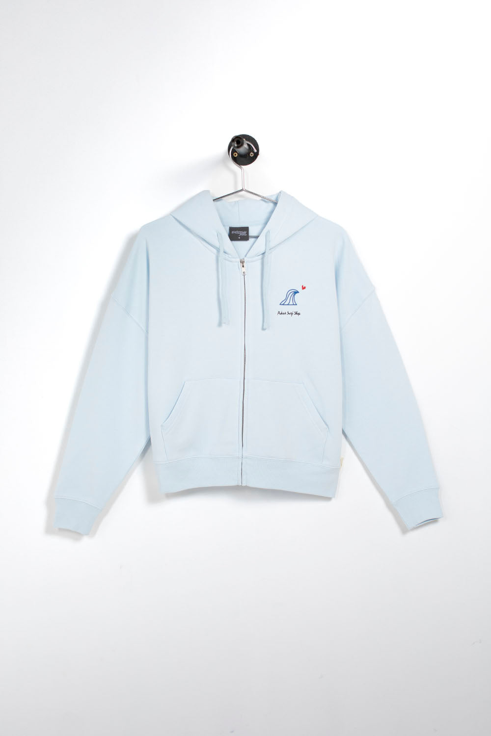 A light blue zip-up hoodie with a drawstring hood and kangaroo pockets, hanging on a white wall. It features a small embroidered logo on the left chest depicting a blue fish with a red star and the text 'FISHING BY JAY'.