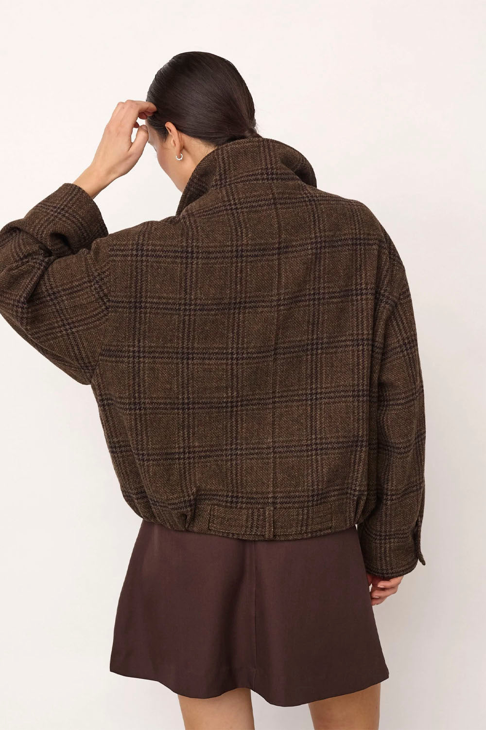 A model shown from the back wearing a brown plaid cropped jacket and a matching brown skirt against a plain off-white background.