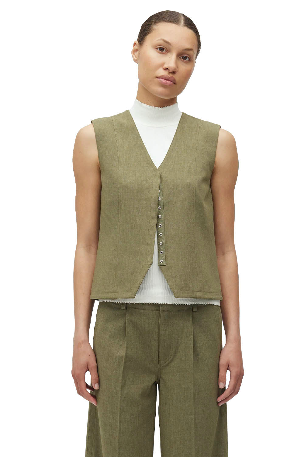 Woman wearing a green vest over a white turtleneck on a white background