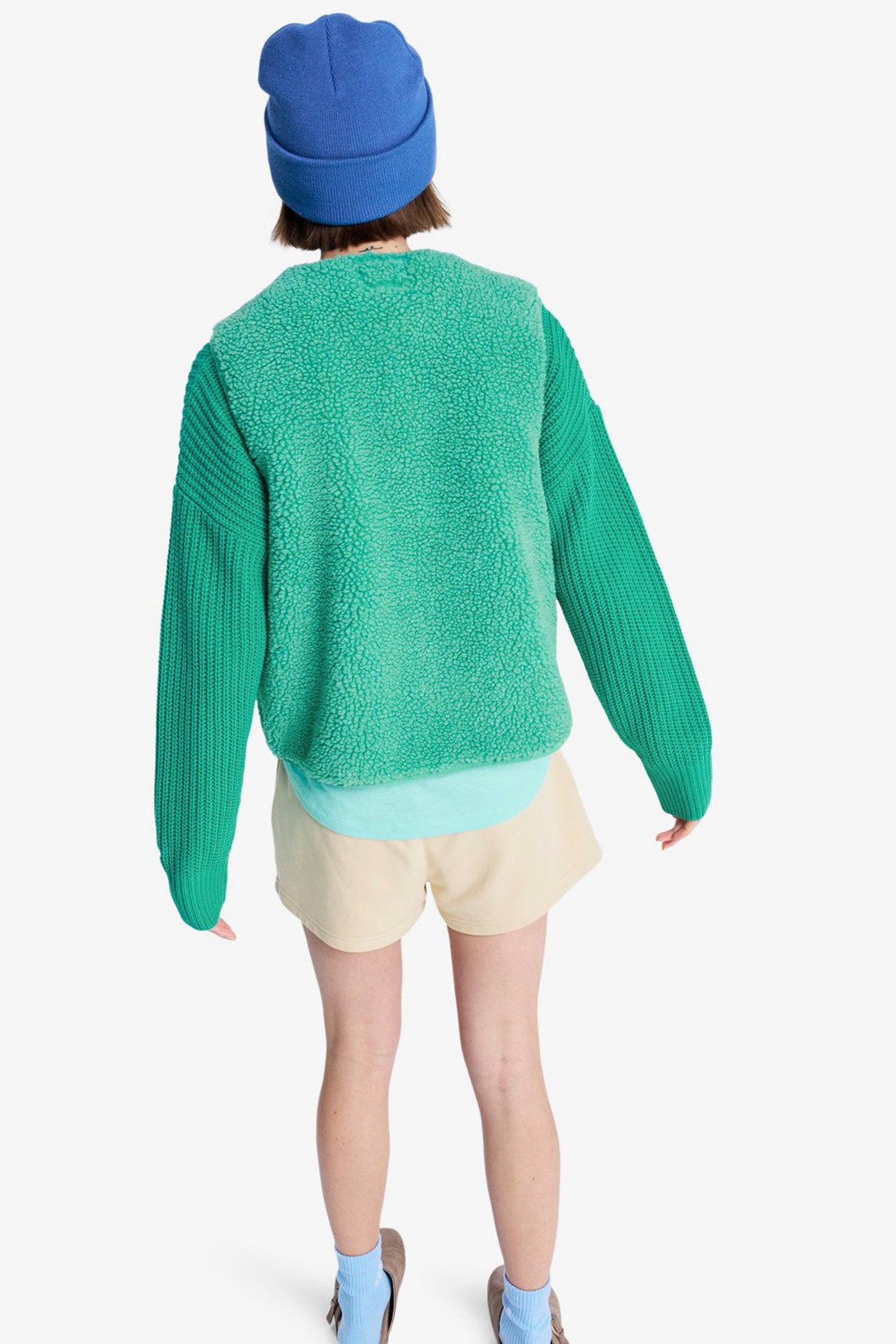 Person wearing a green ROXY Iconic Town vest, blue beanie, light shorts, and blue shoes on a white background