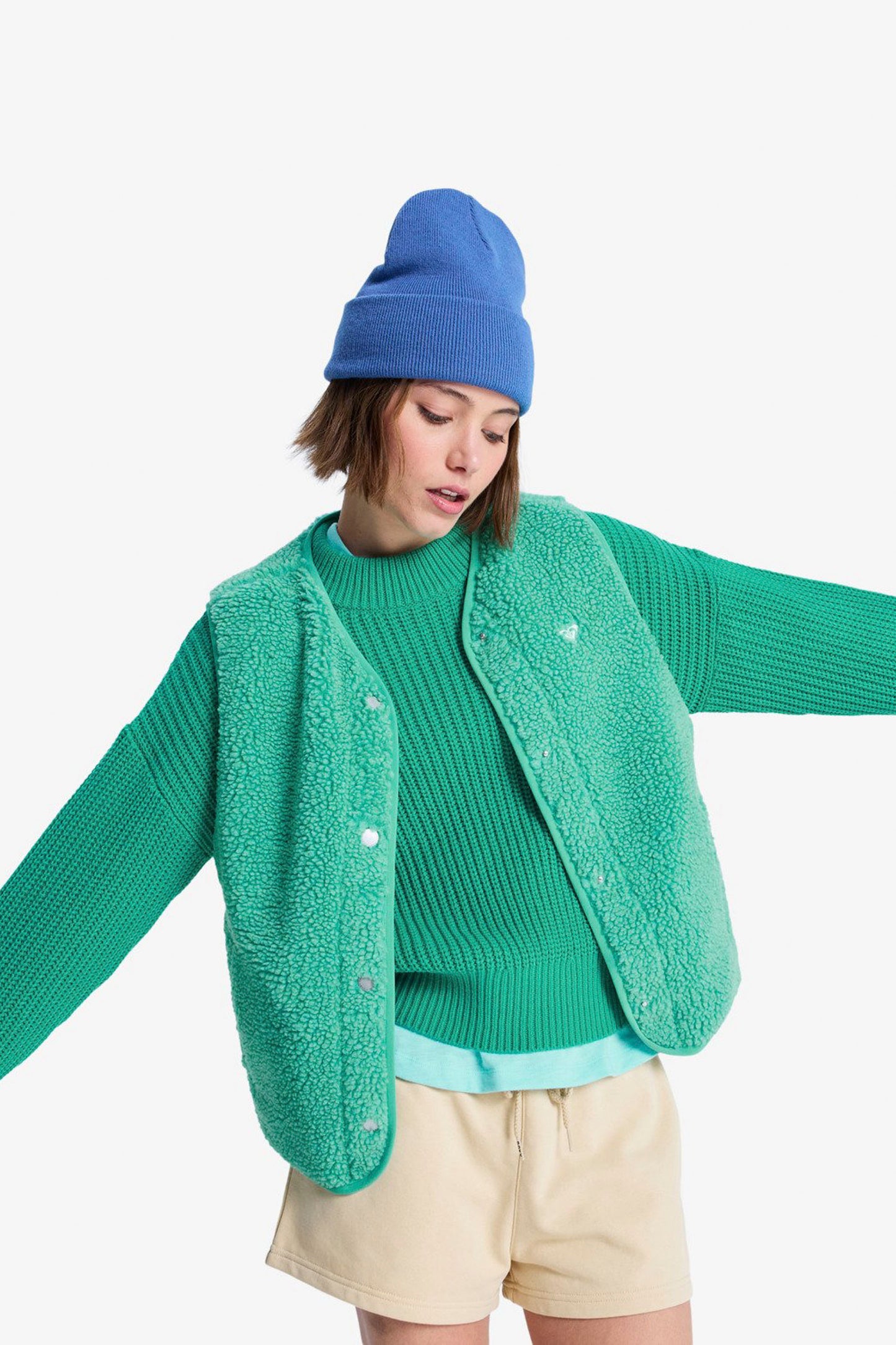 Person wearing a green ROXY Iconic Town vest, blue beanie, and beige shorts on a white background