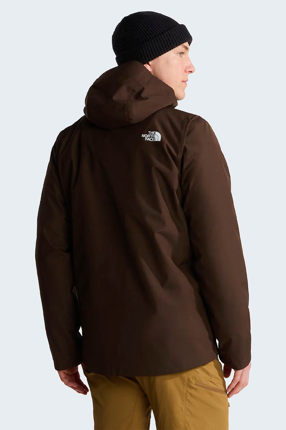 A man wearing a dark brown hooded jacket by The North Face, shown from the back. He is also wearing a black beanie and tan pants against a light gray studio background.