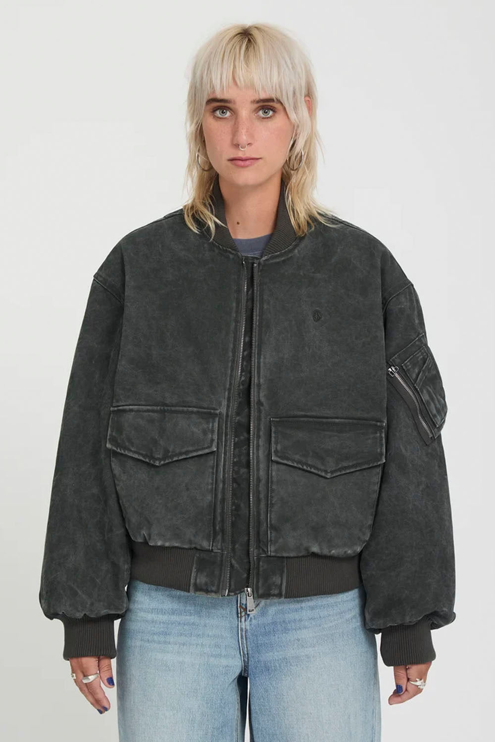 A model wearing a washed black bomber jacket with front flap pockets and ribbed trim, paired with light blue jeans, against a plain light gray background.