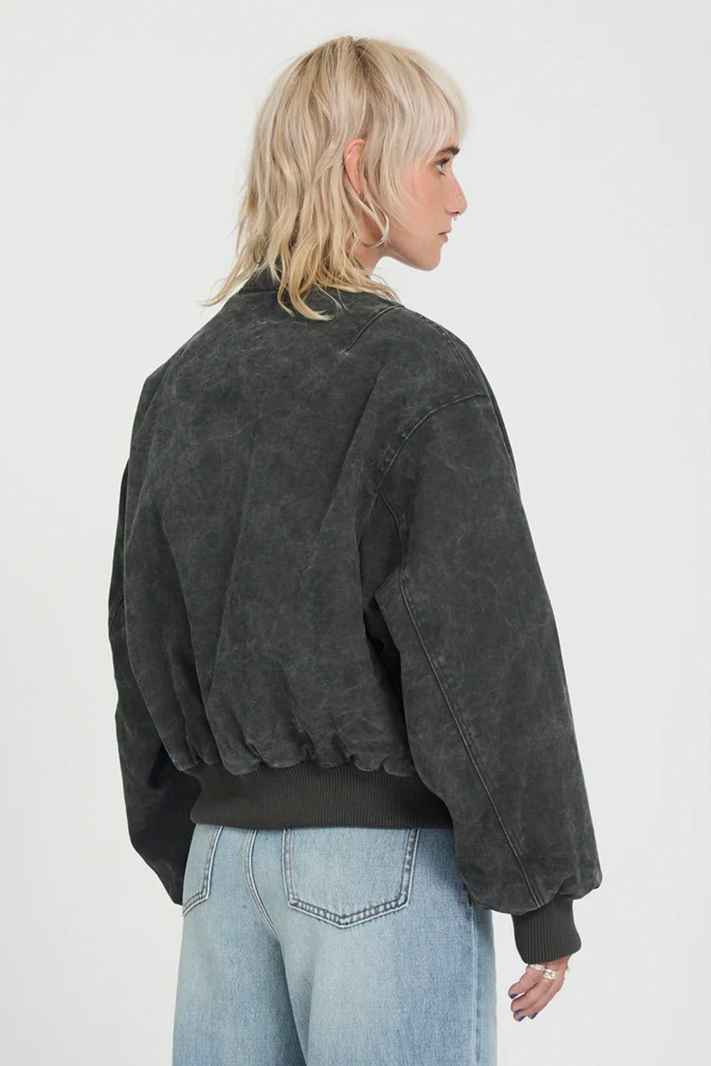 A model shown from the back wearing a washed black bomber jacket and light blue jeans against a plain white studio background.