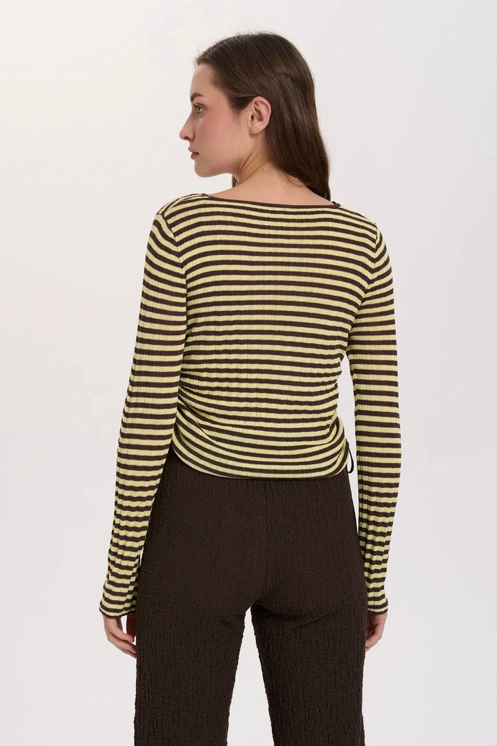 A woman shown from the back wearing a long-sleeve ribbed knit top with horizontal olive green and beige stripes, paired with dark brown pants, against a plain white studio background.
