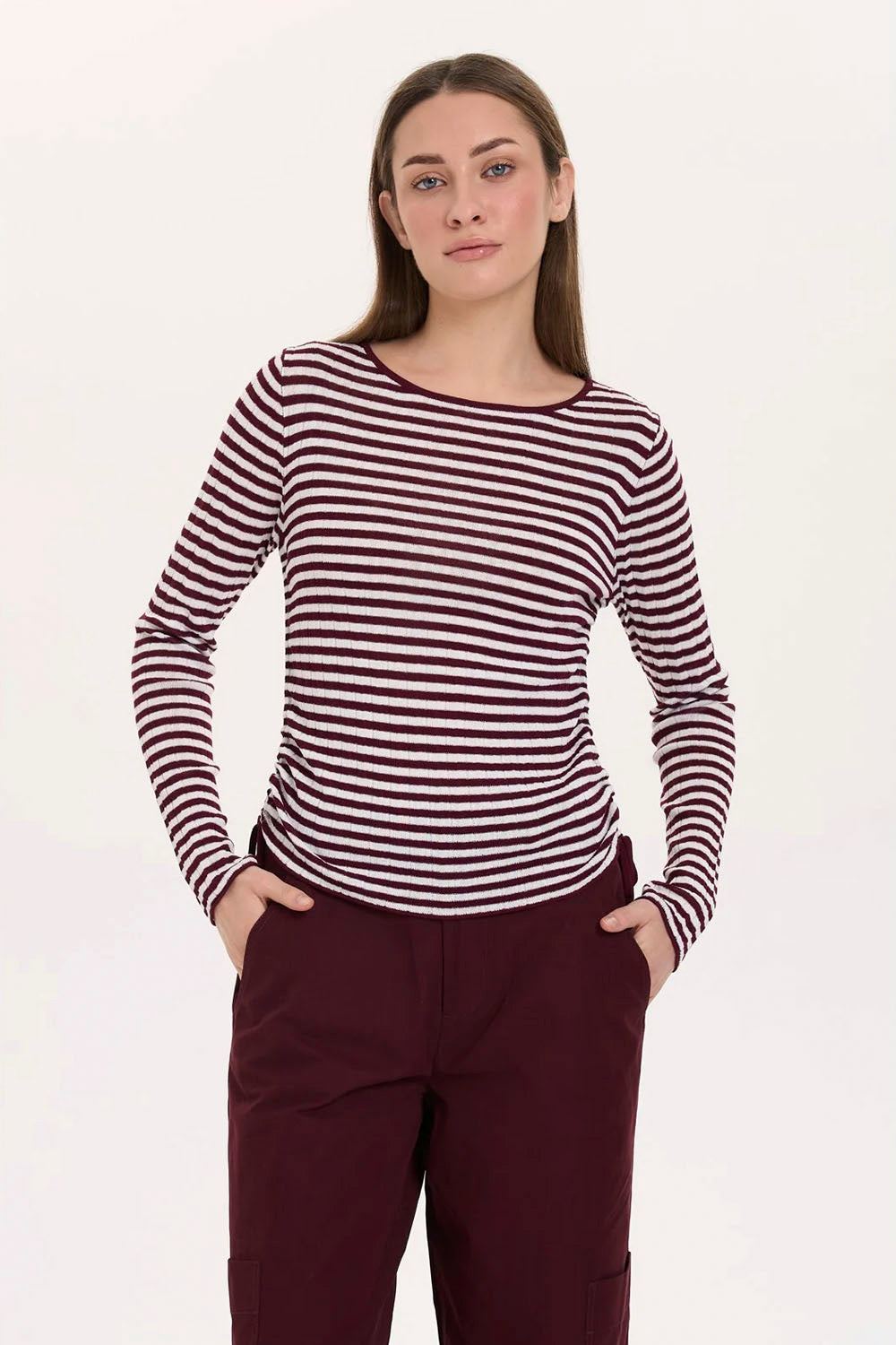 A woman modeling a long-sleeve crew-neck top with horizontal burgundy and white stripes, paired with burgundy pants, against a plain white studio background.