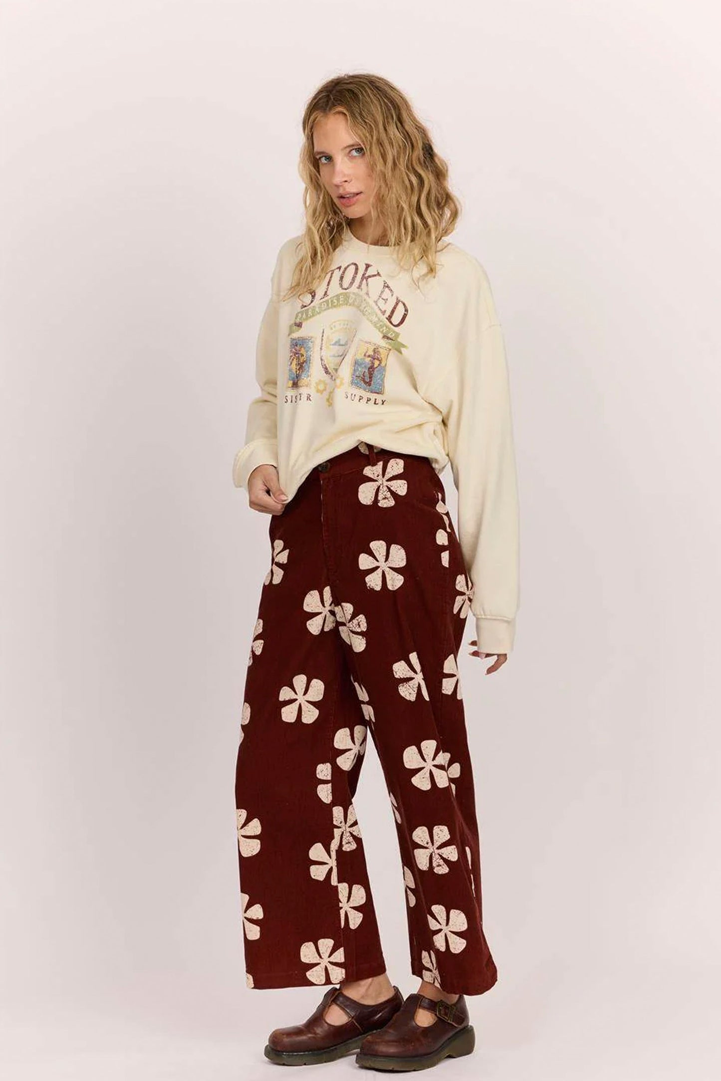 Sisstrevolution Pukas Surf Shop Person wearing a cream sweatshirt with text and maroon pants