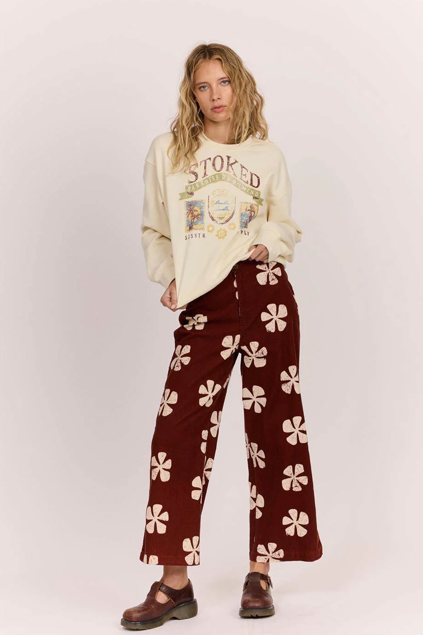 Sisstrevolution Pukas Surf Shop Person wearing a cream sweatshirt with text and maroon pants