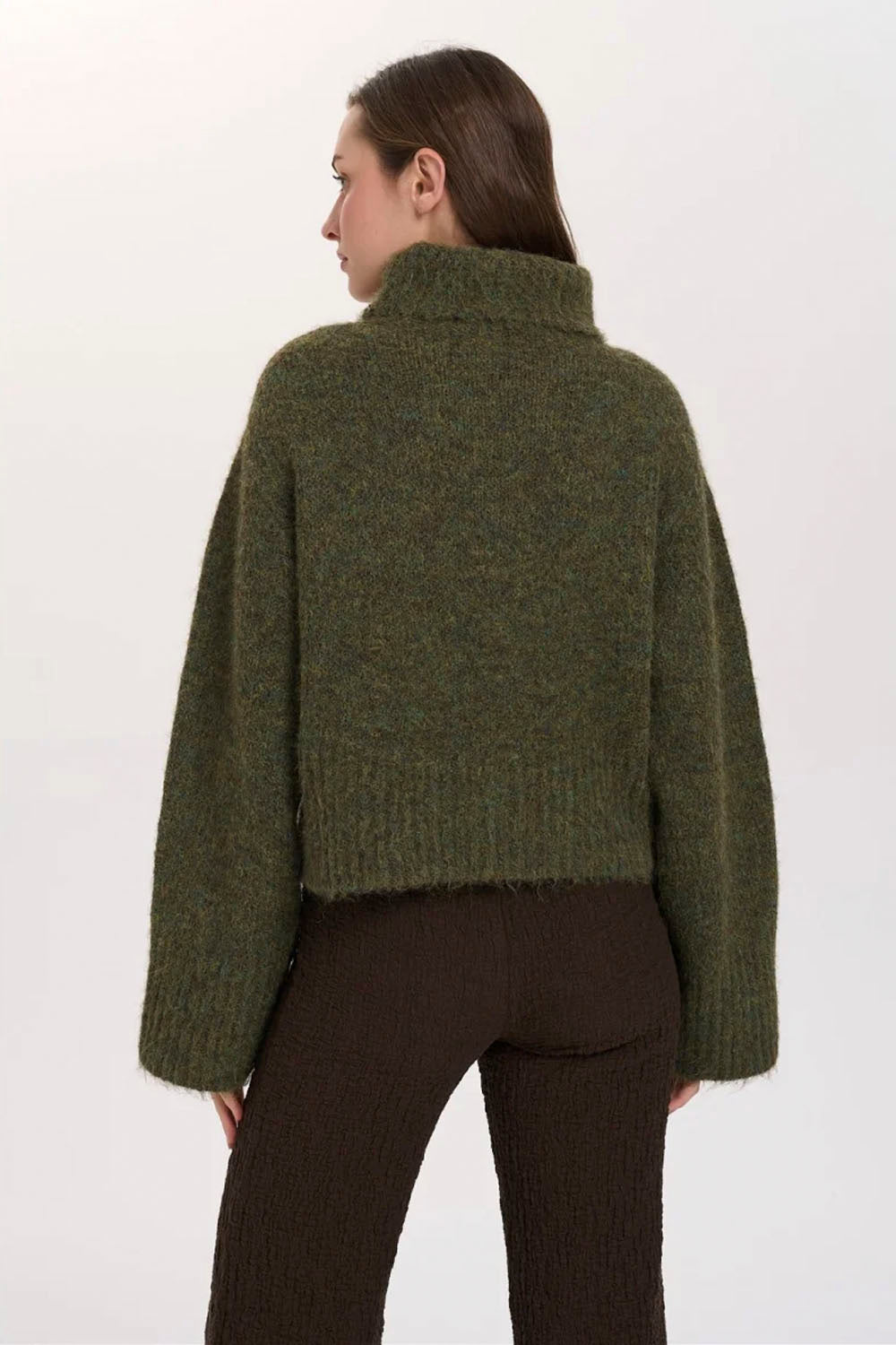 A woman shown from the back wearing a cropped, long-sleeve knit sweater in a heathered olive green color, paired with dark brown pants, against a plain white studio background.