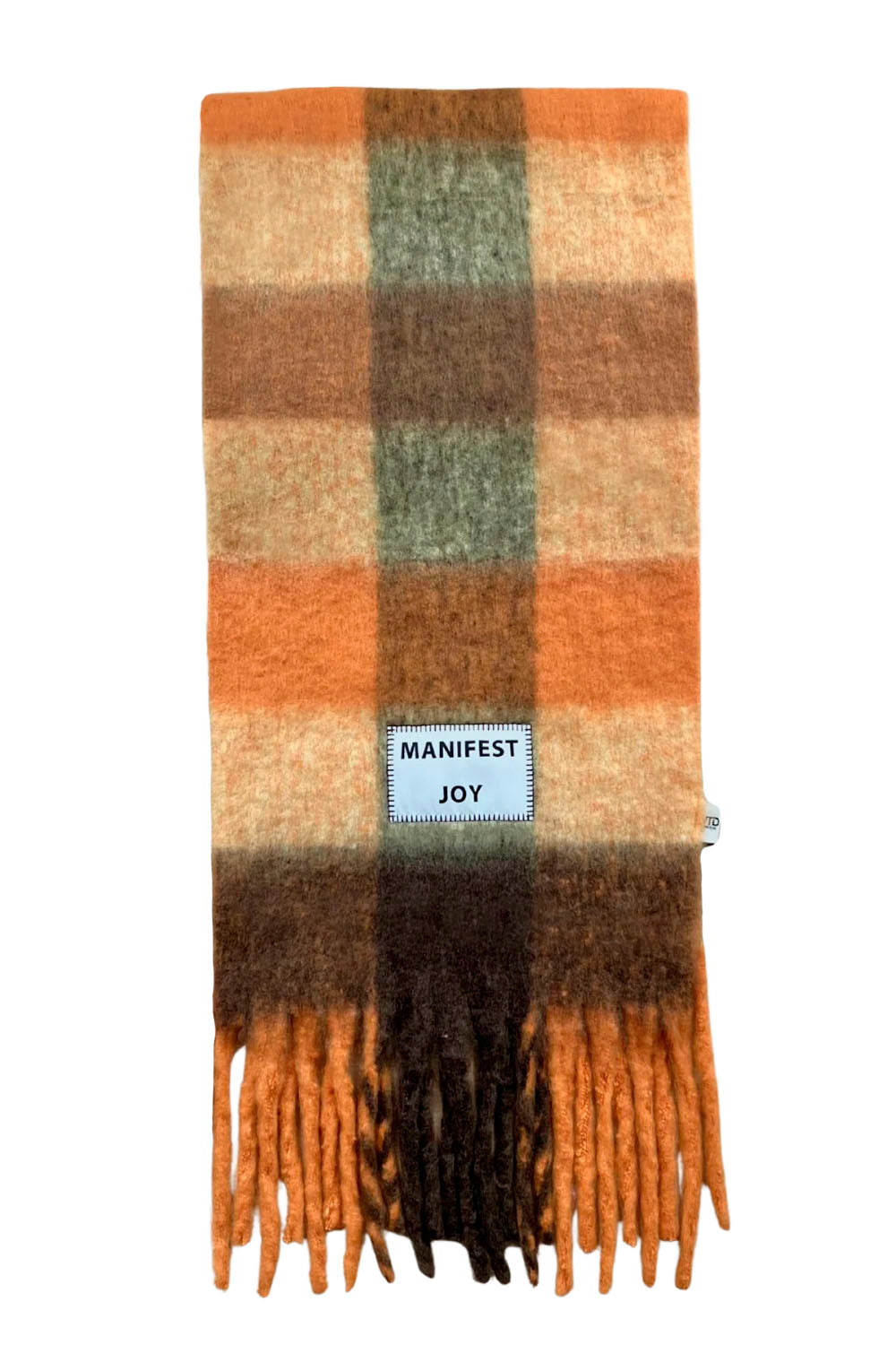 A plaid fringed scarf in shades of orange, brown, beige, and muted green, featuring a light blue label that reads 'MANIFEST JOY'.