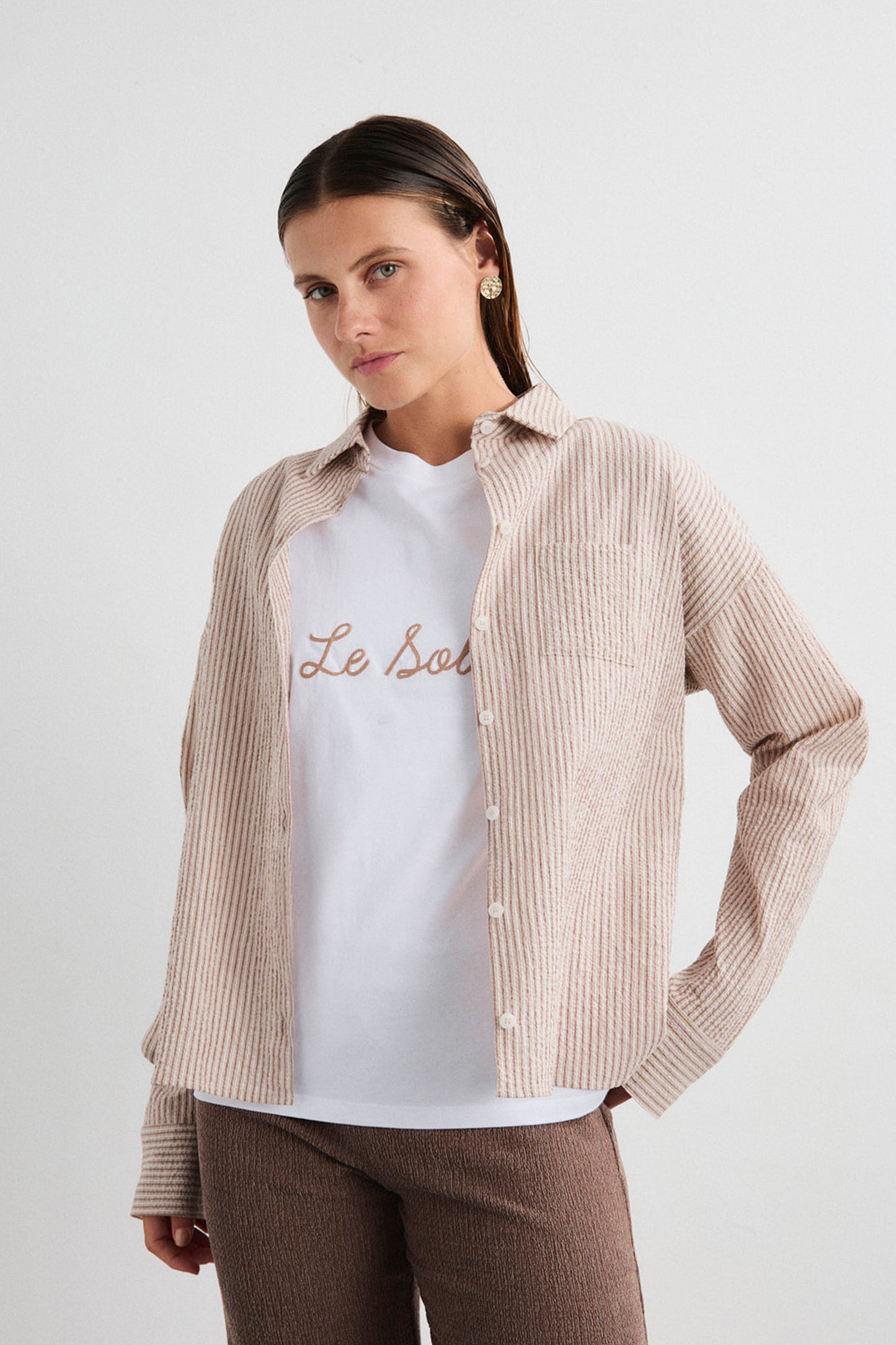 Woman wearing a beige checkered shirt over a white t-shirt with text, on a plain background