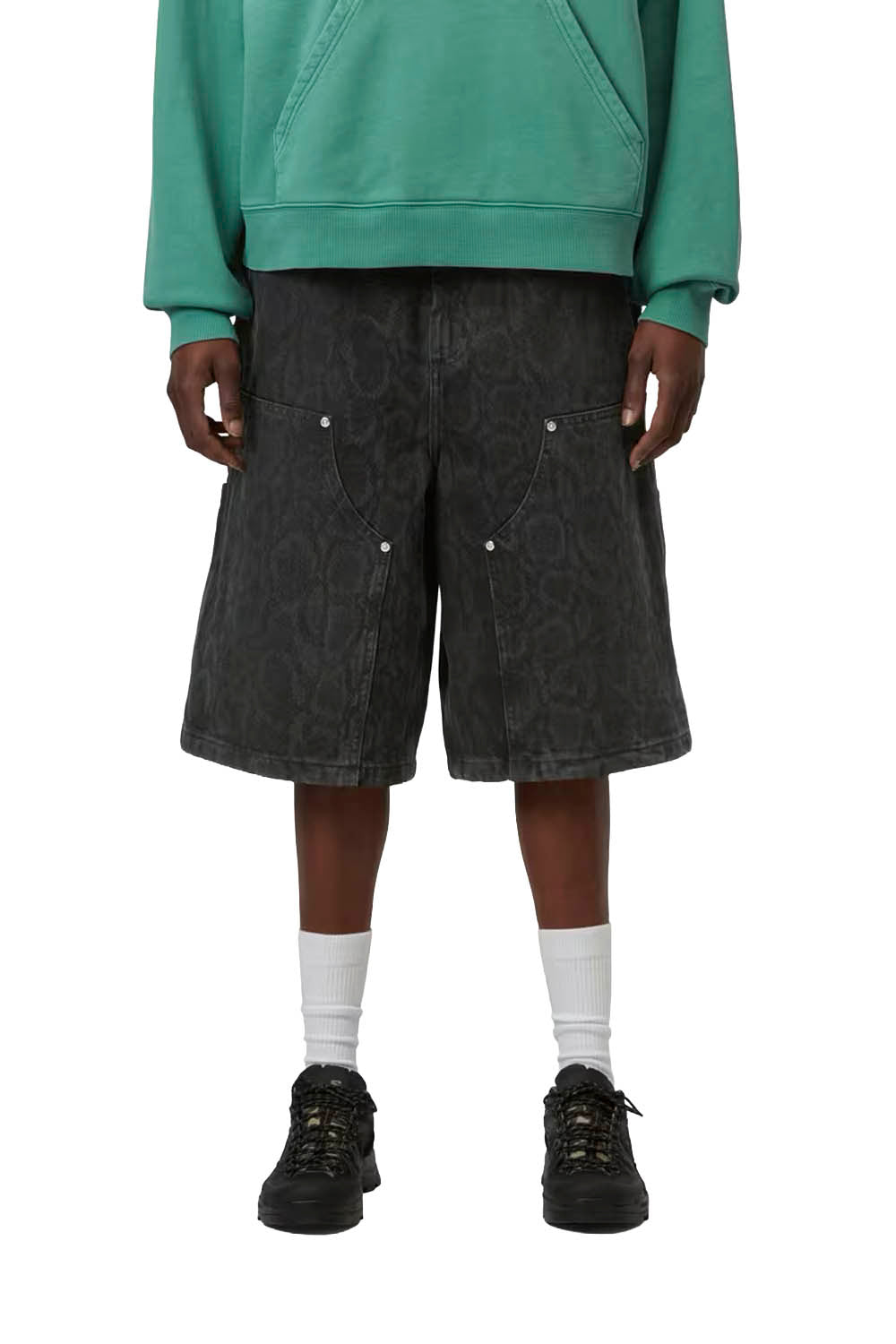 Woman wearing black denim shorts, a green hoodie, white socks, and black shoes on a white background