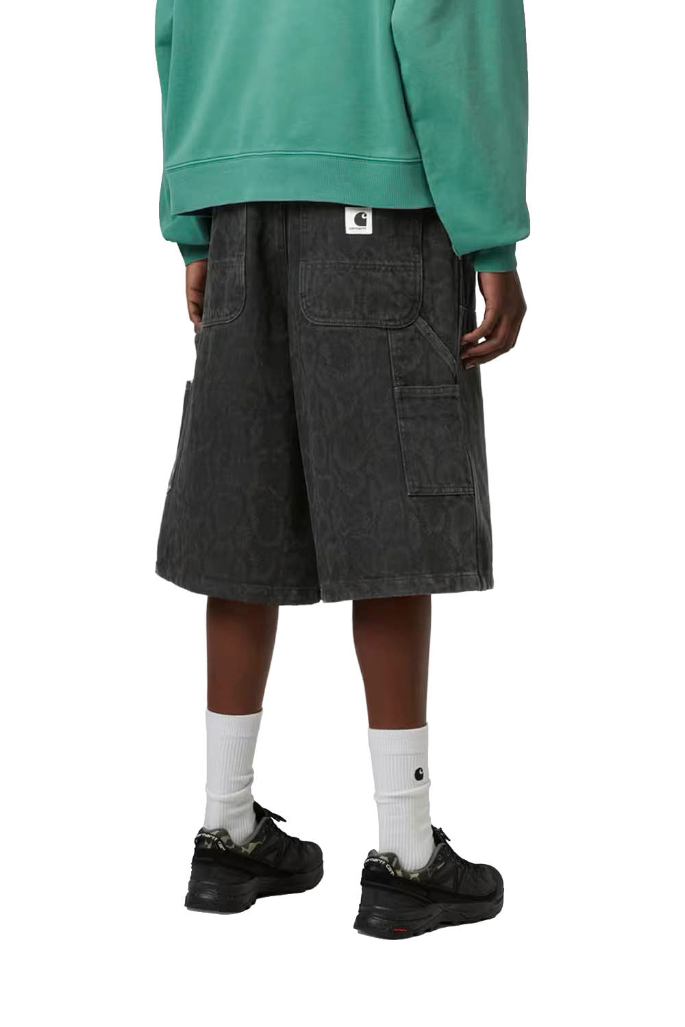 Woman wearing black denim shorts, a green hoodie, white socks, and black shoes on a white background