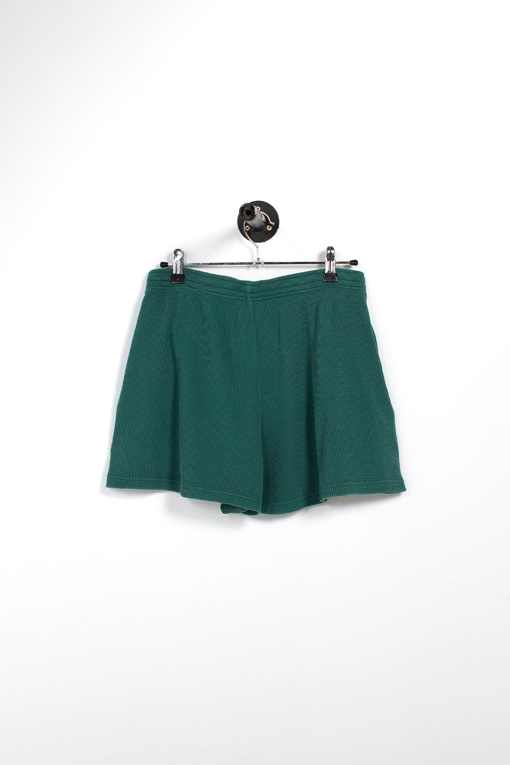A pair of dark green shorts hanging from a metal hanger against a plain white background.