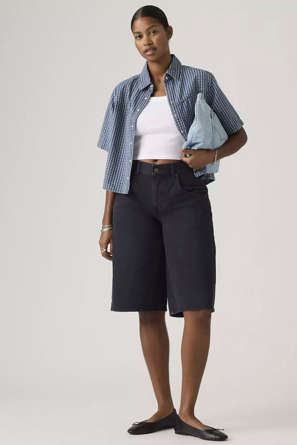 Woman wearing a blue checkered shirt over a white top with black shorts on a white background