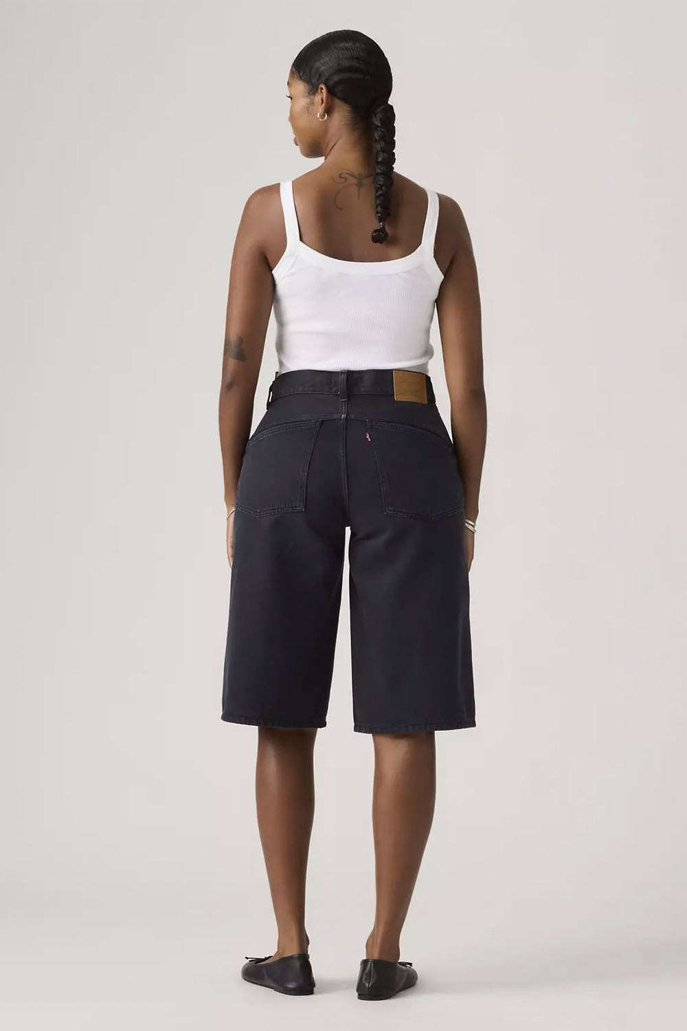 Person wearing black shorts and a white tank top on a plain background