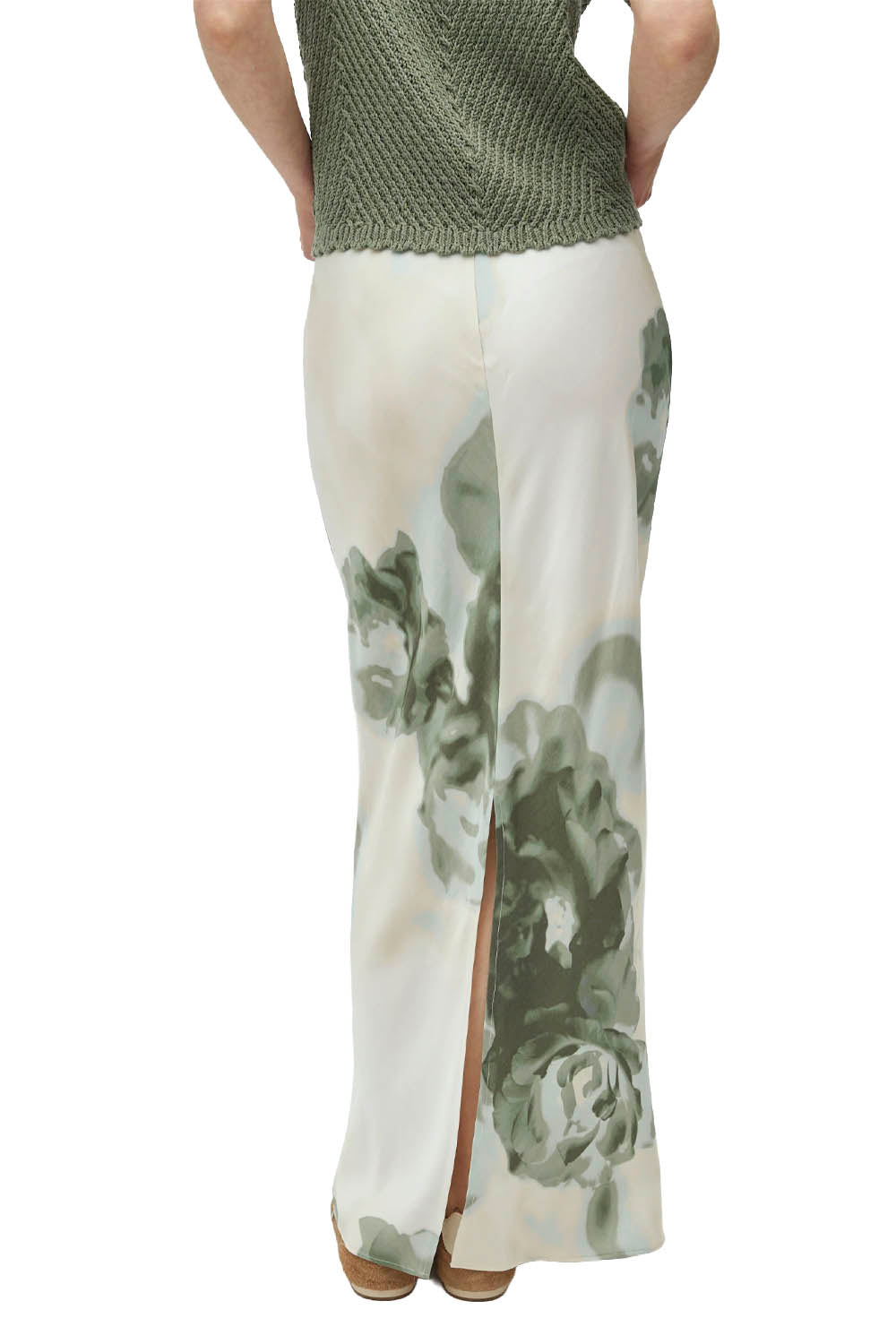 Woman wearing a green knitted top and white pants with floral pattern on a white background